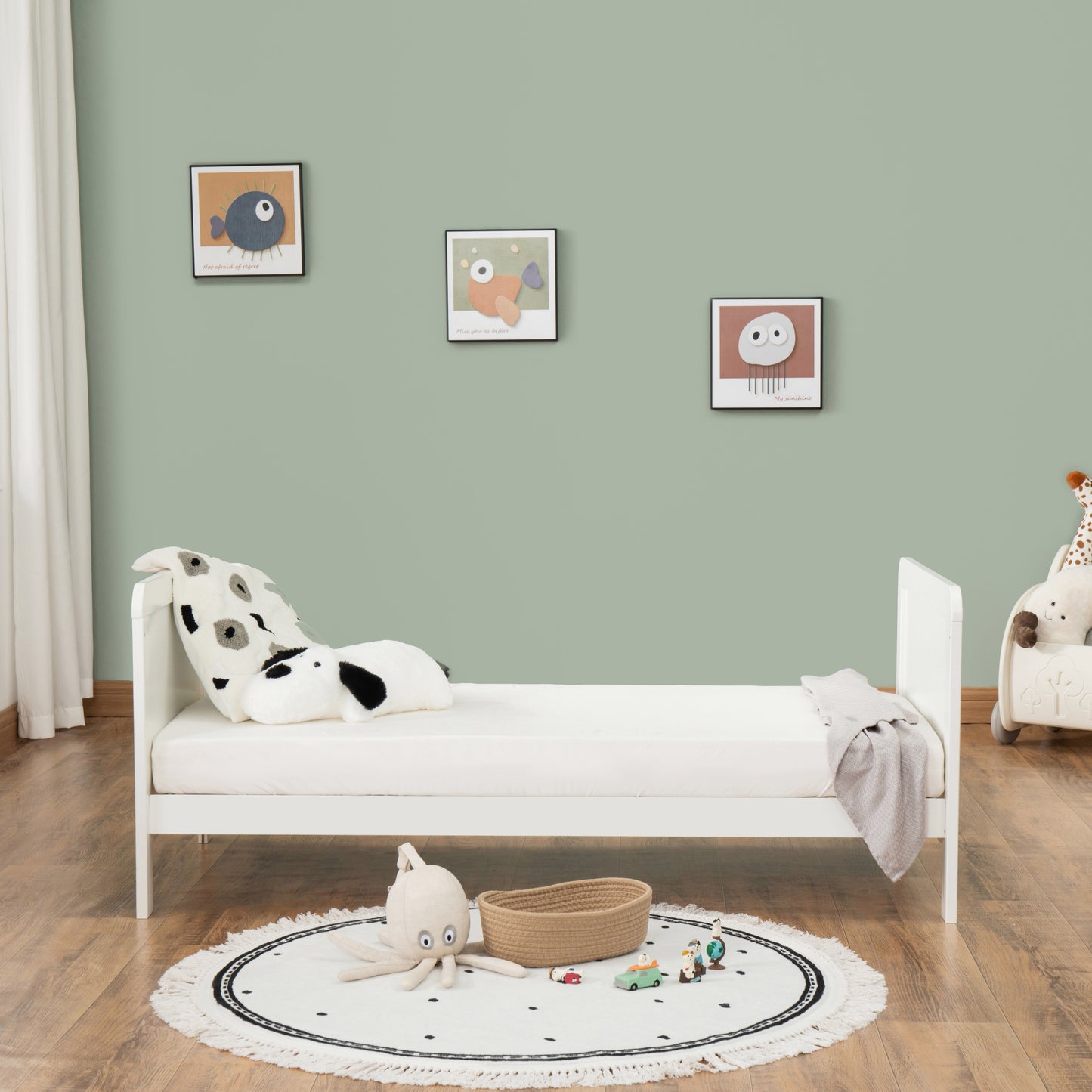Children's bedroom with a white bed, toys, and framed pictures on a green wall.