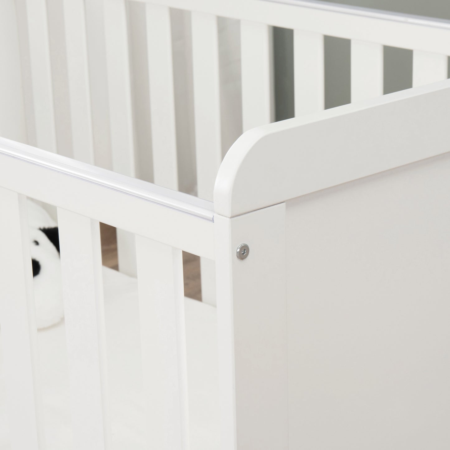 Close-up of a white cot with a teething rail with a neutral background