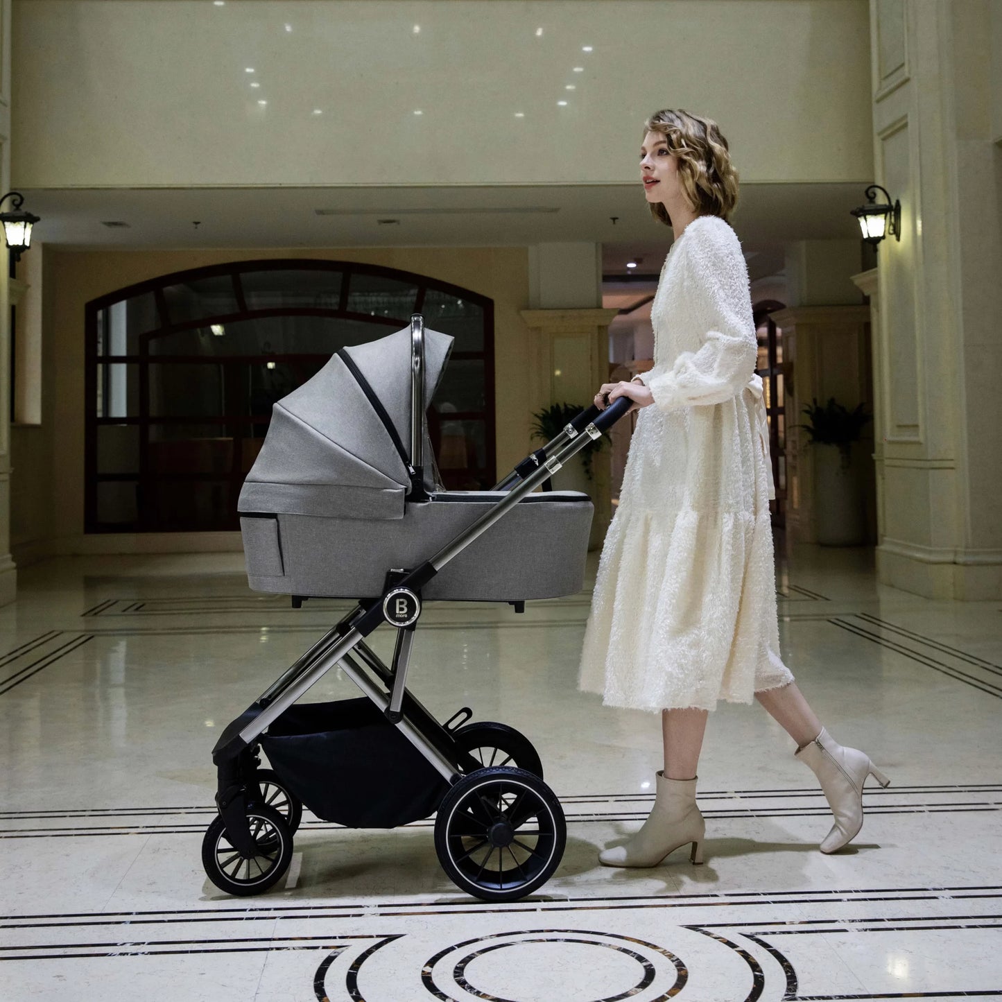 Woman in a white dress pushing a baby stroller in an elegant hallway.
