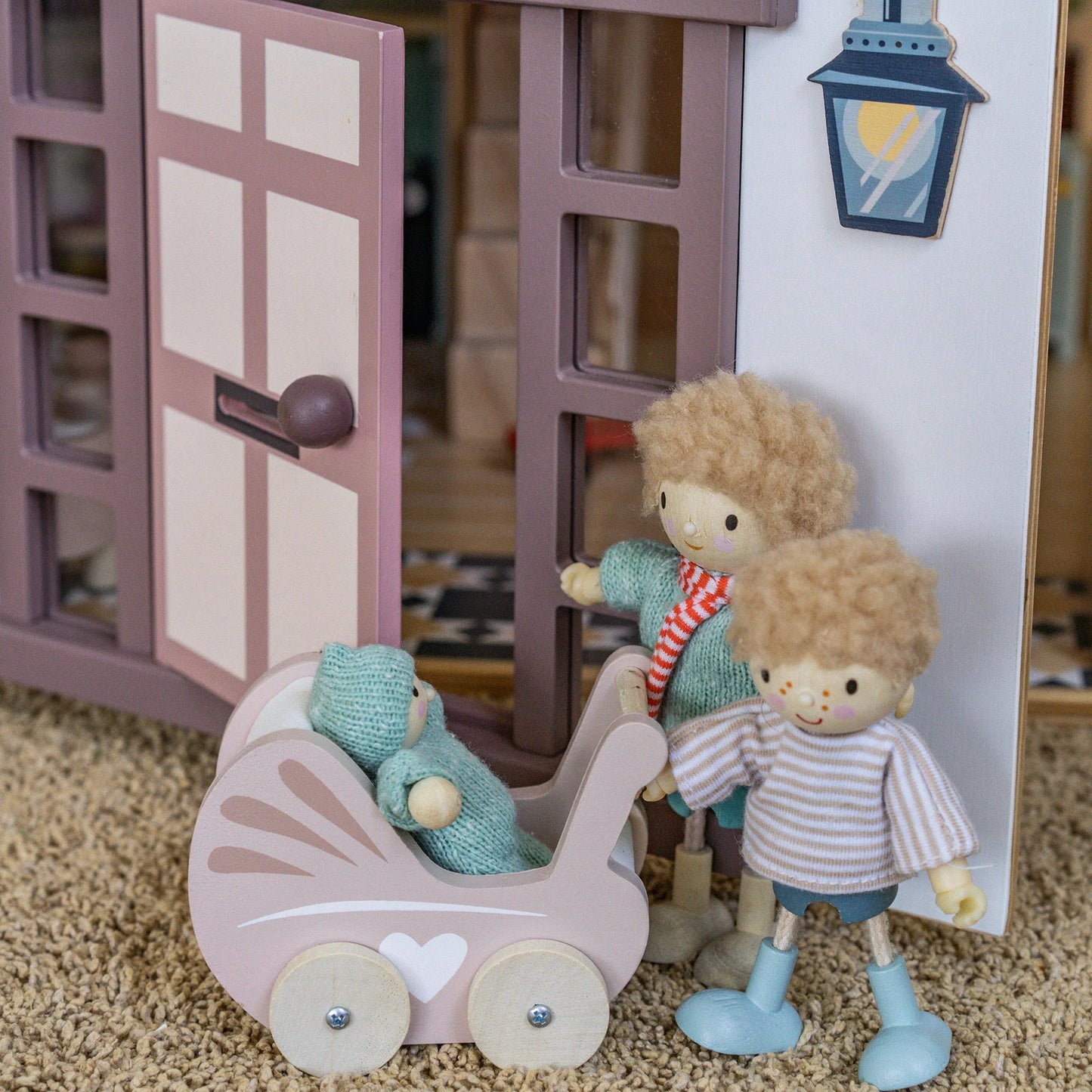 Toy dolls with a baby carriage in front of a toy house