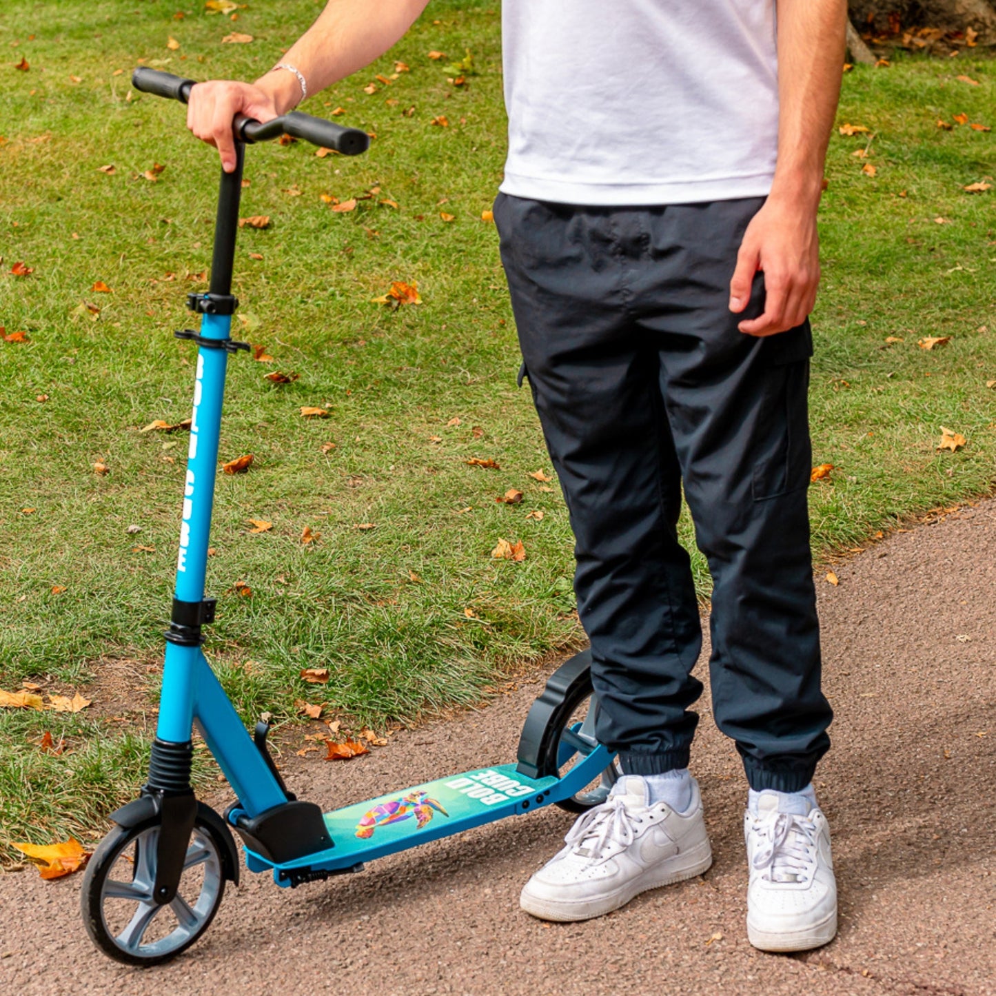 Person holding a blue scooter on a grassy path