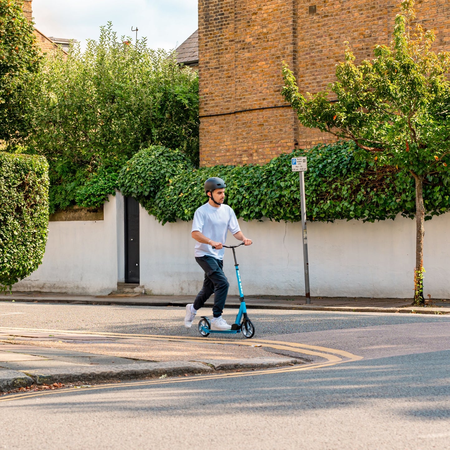 Man riding a scooter on a street with greenery and buildings in the background