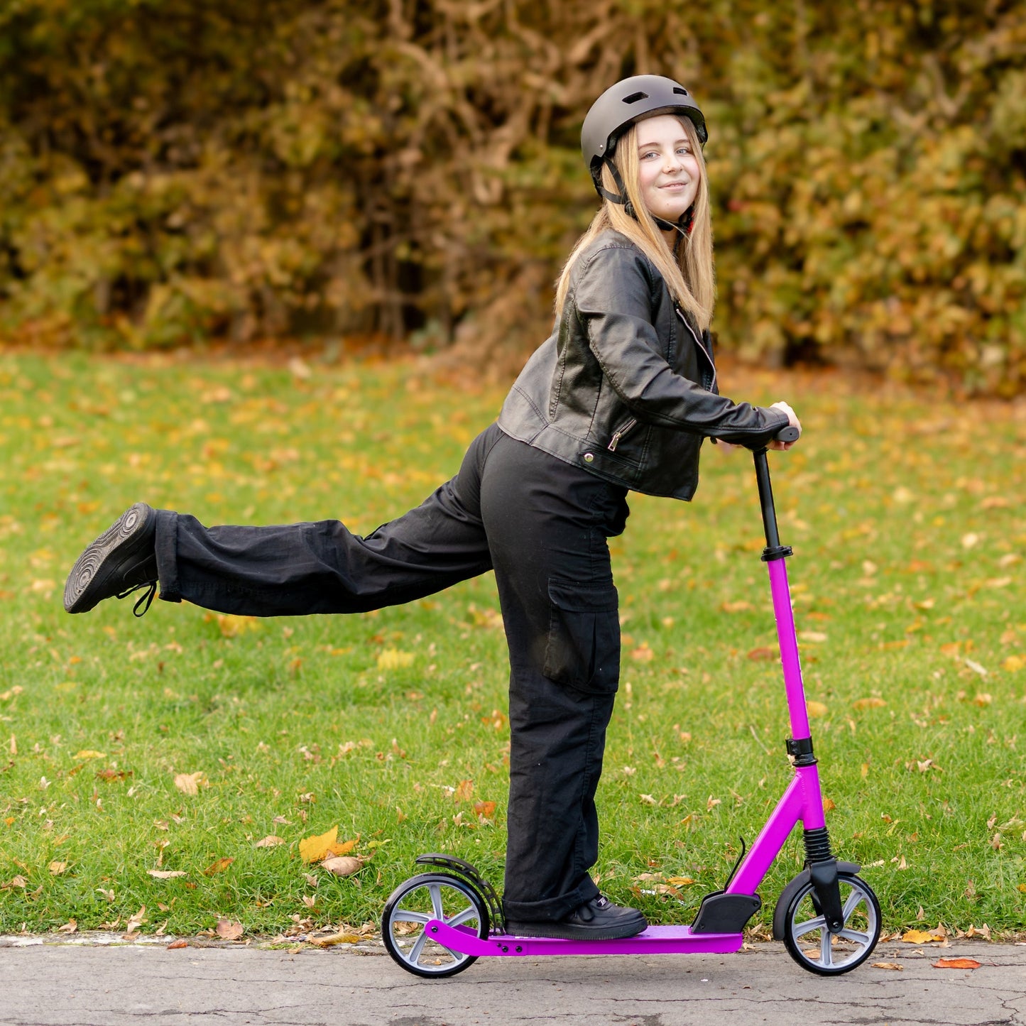 Person riding a pink scooter outdoors on a grassy area with trees in the background