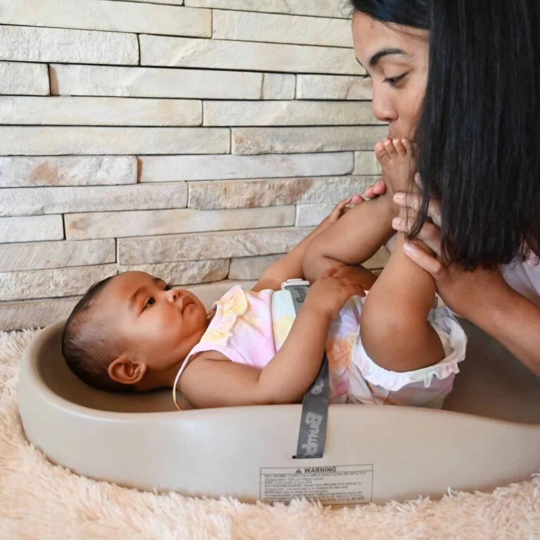 Baby lying in a basin with a woman beside it against a stone wall background