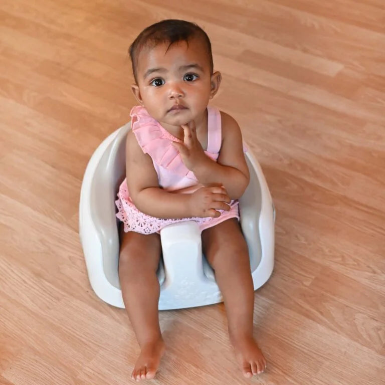 Baby sitting in a white baby seat on a wooden floor