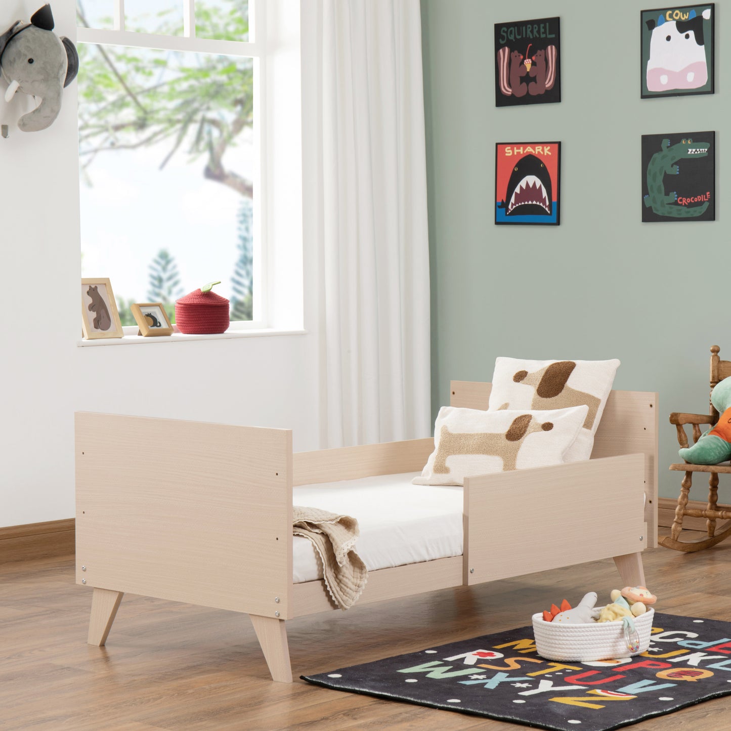Children's bedroom with a wooden toddler bed, colorful rug, and wall art.