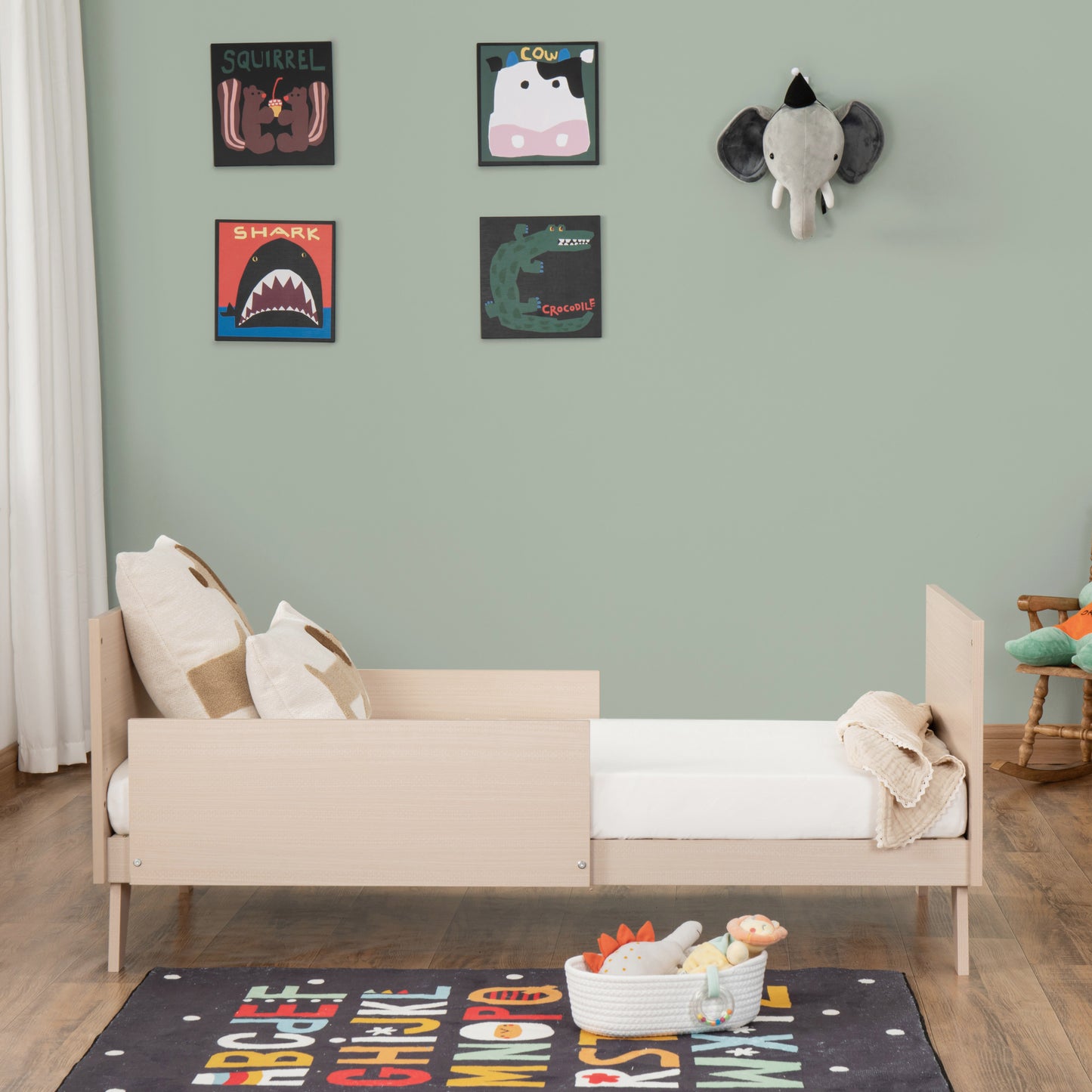 Children's room with a wooden toddler bed, colourful posters on the wall, and toys on the floor.