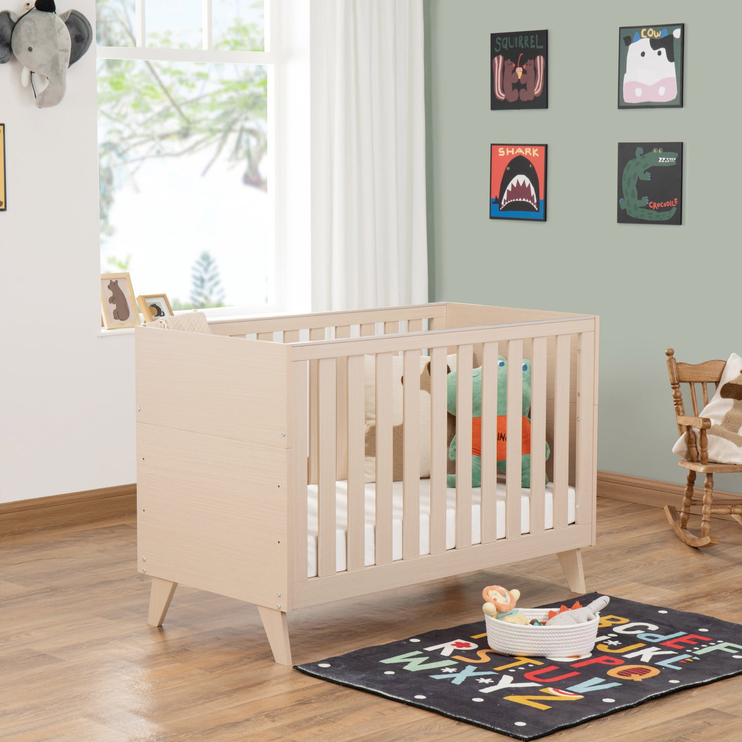 Nursery room with a cot, colourful rug, and toys on a wooden floor.