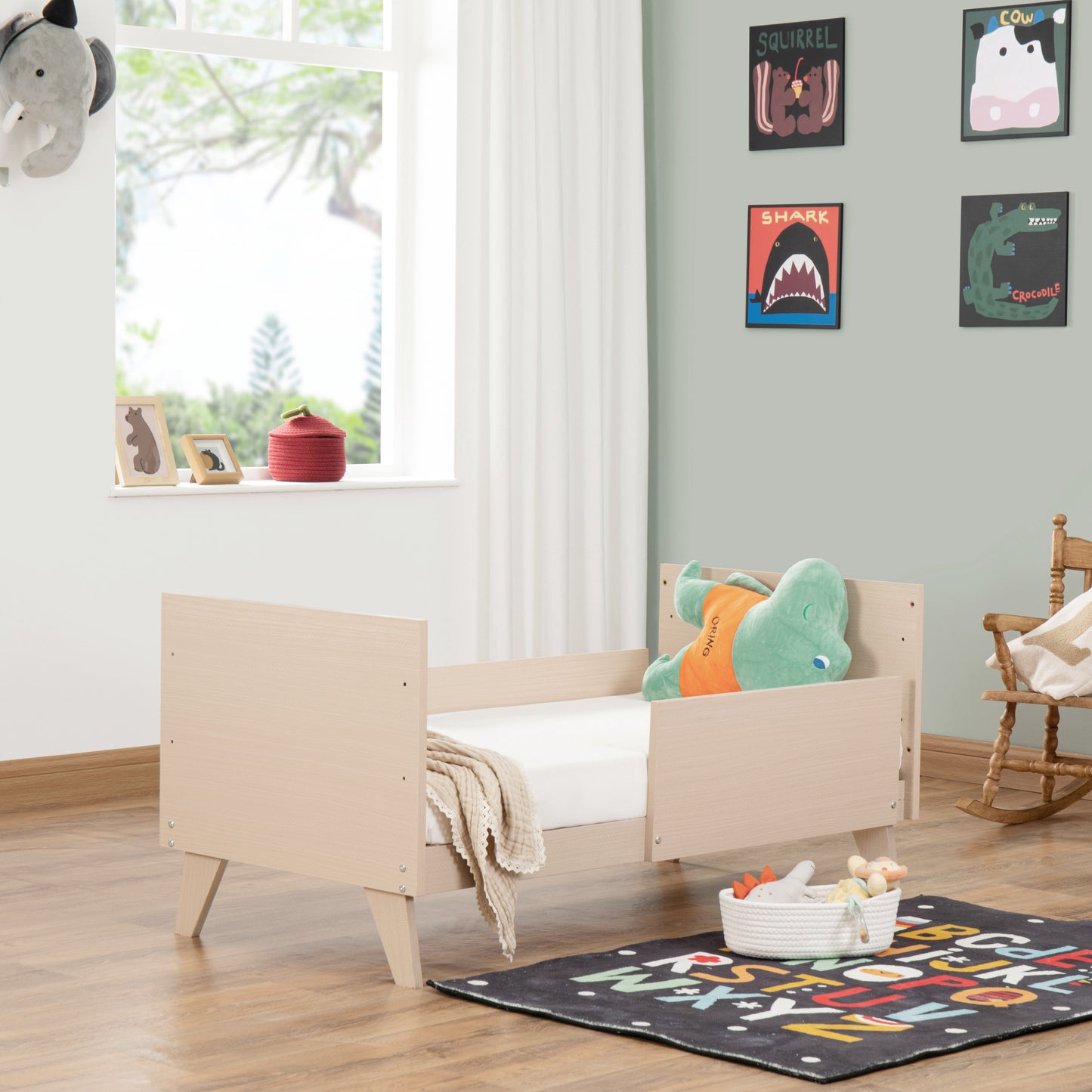 Children's bedroom with a wooden toddler bed, colourful rug, and wall decorations.