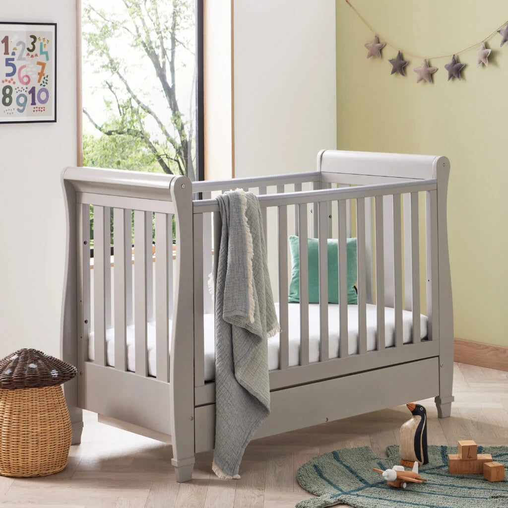 Gray crib in a room with toys and a window