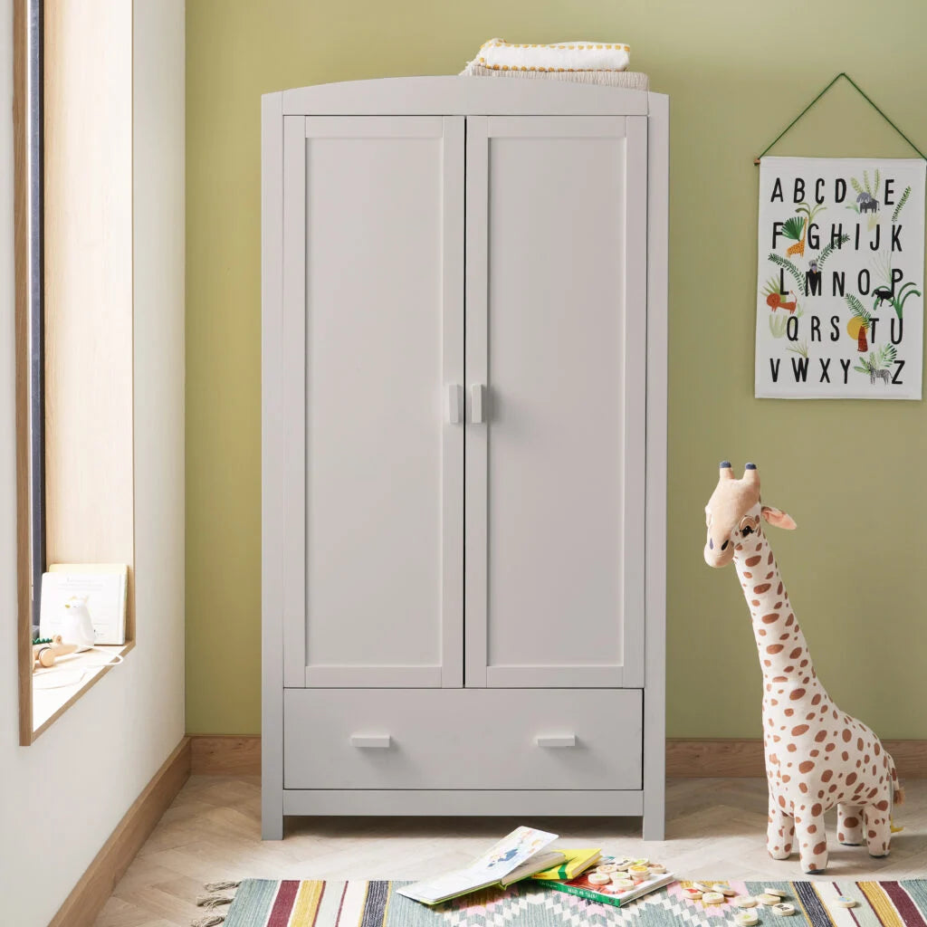 Children's room with a light gray wardrobe, colorful rug, and stuffed giraffe.