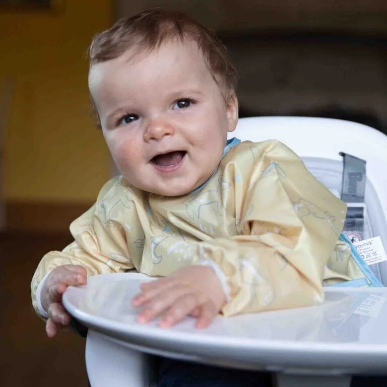 Baby in a high chair wearing a bib with a visible brand label.