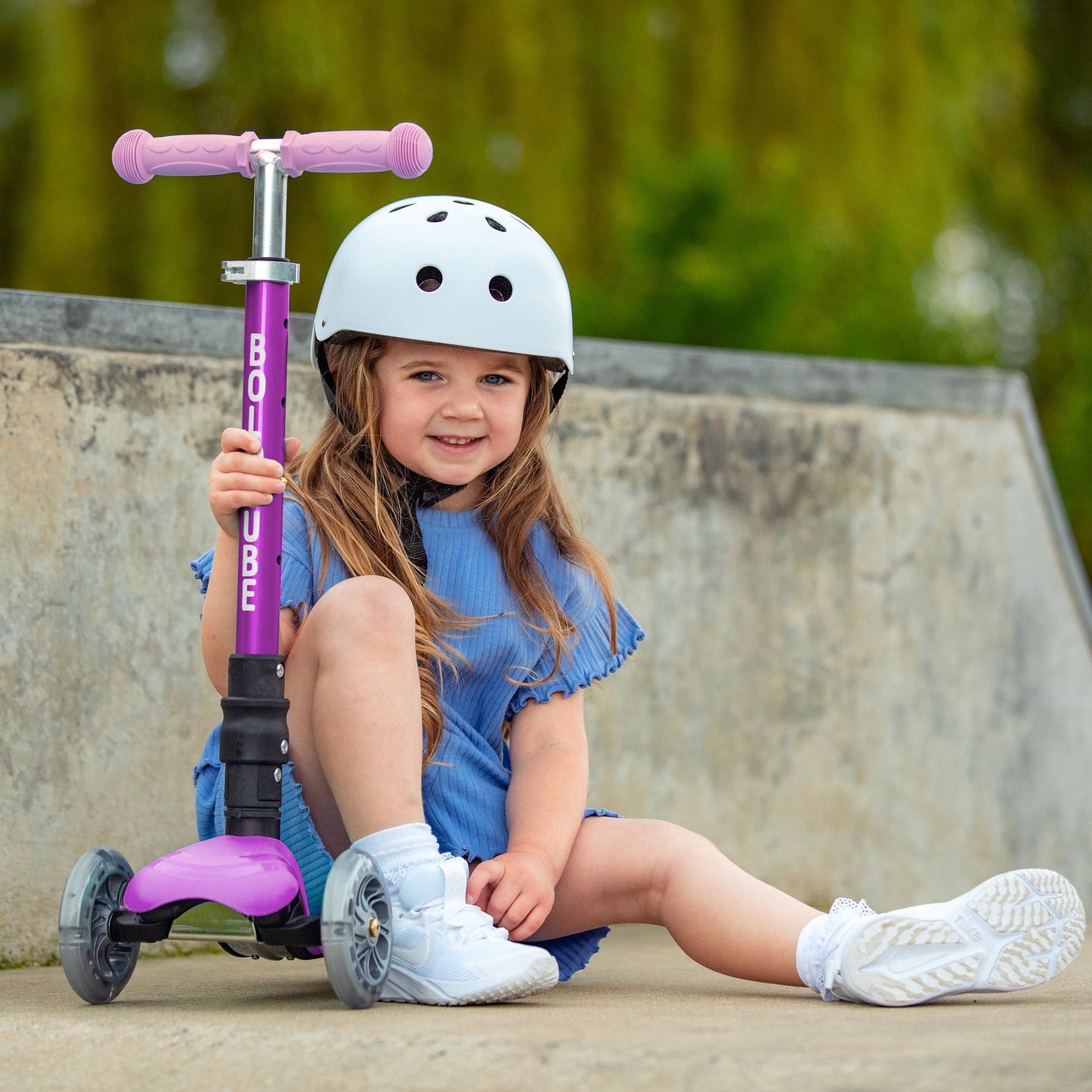 Child sitting on a bench with a purple scooter, wearing a helmet.