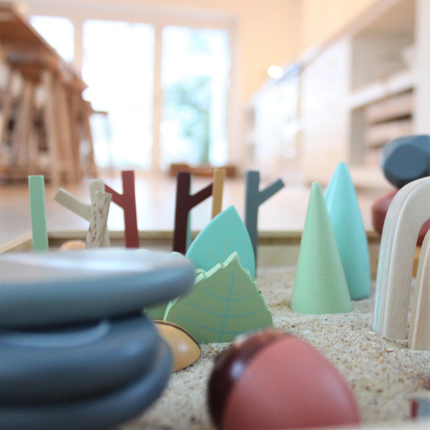 Colorful wooden toys on a sandy surface with a blurred indoor background
