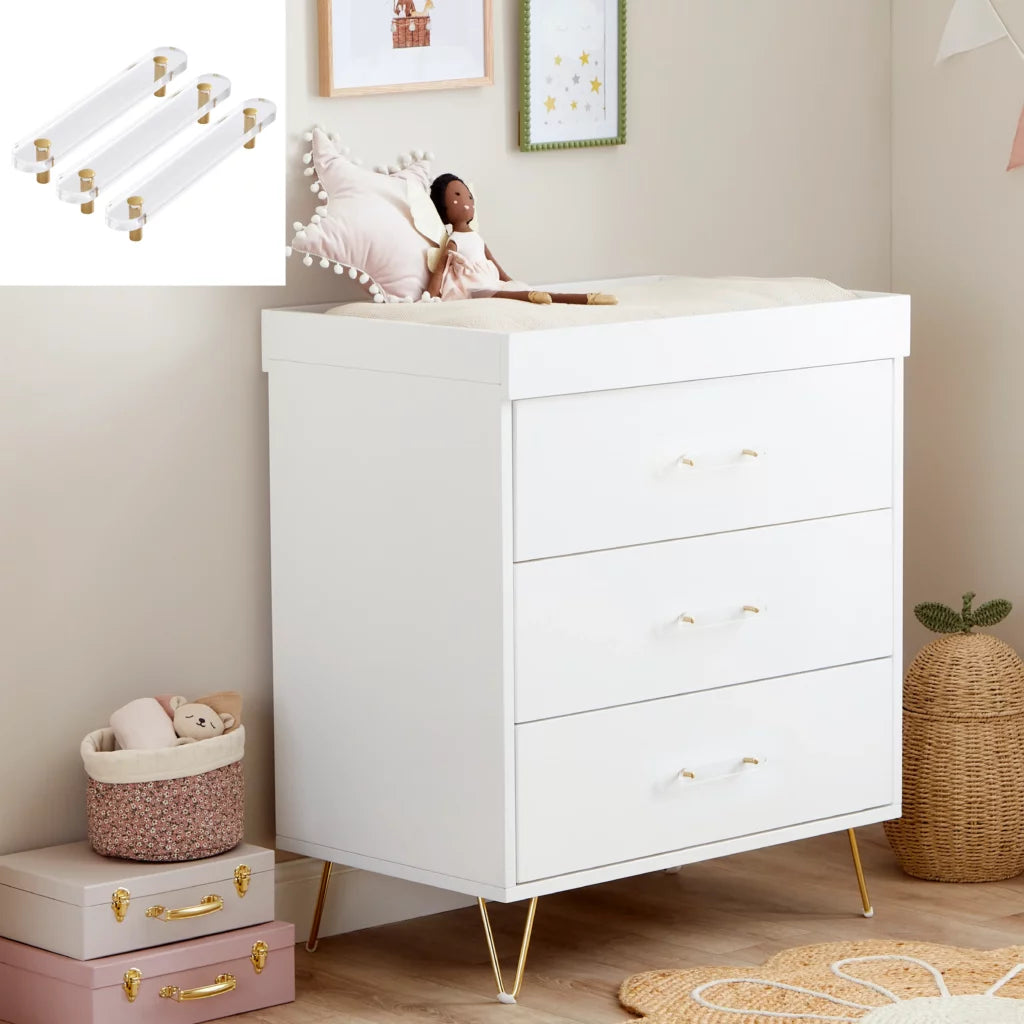 White dresser with gold legs in a nursery setting with toys and decor.
