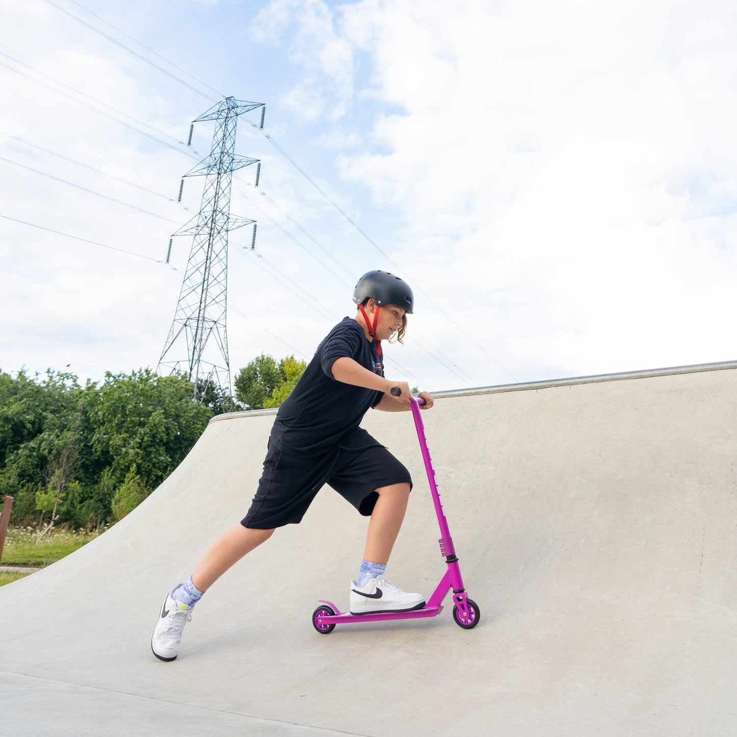 Person riding a pink scooter on a concrete ramp with a clear sky and power lines in the background