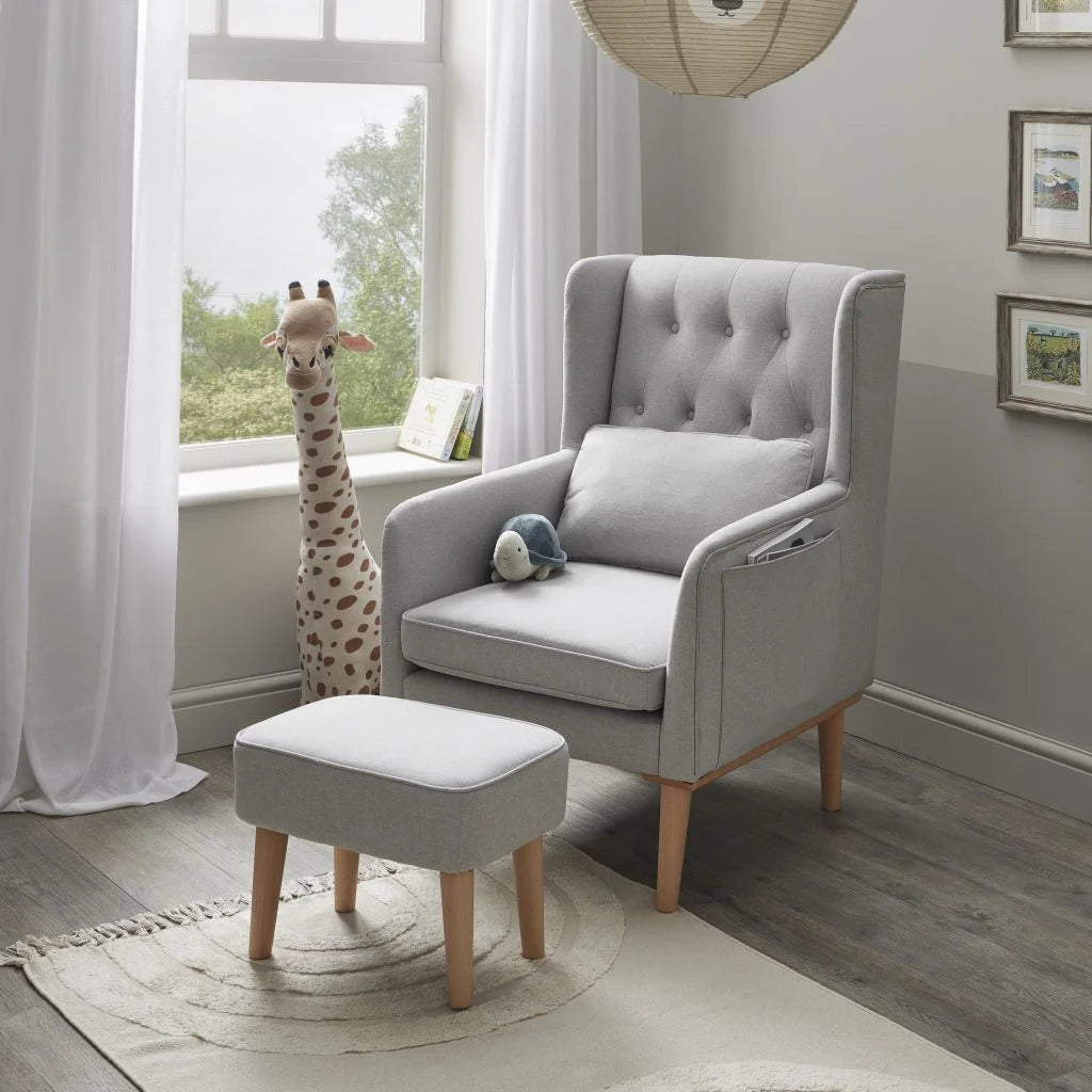 Gray armchair with ottoman in a room with large windows and decorative elements.