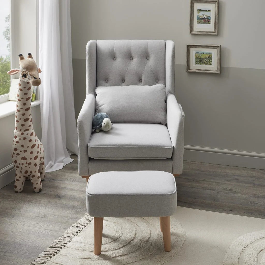 Gray upholstered chair with ottoman in a room with a window and framed pictures on the wall.