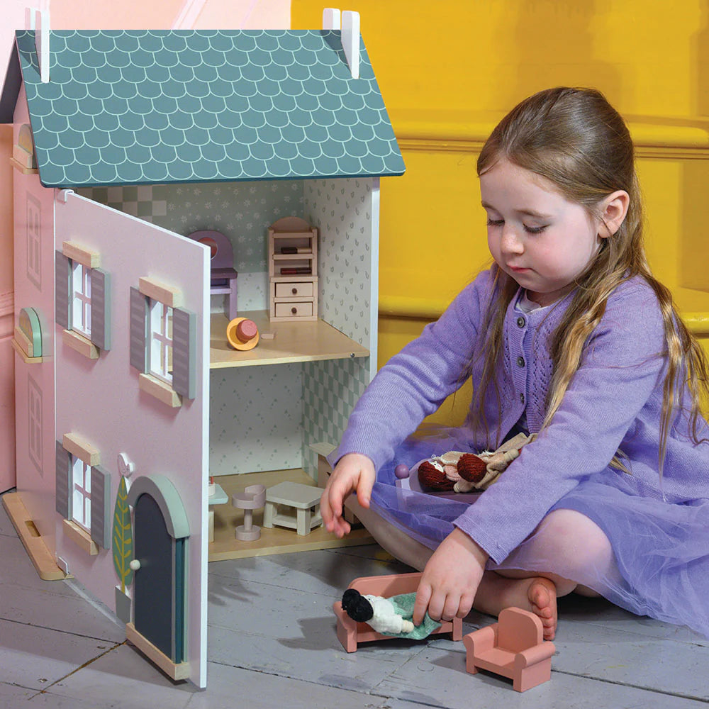 Child playing with a dollhouse and toys on a wooden floor.
