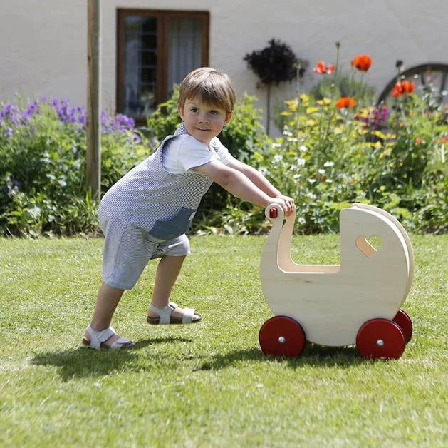 Child pushing a wooden toy carriage in a garden