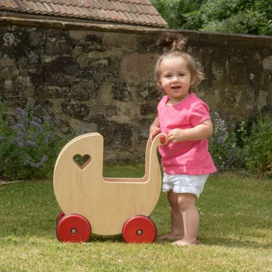 Child pushing a wooden doll pram outdoors near a stone wall.