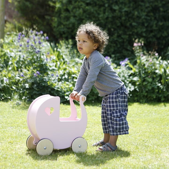 Child pushing a pink toy pram in a garden