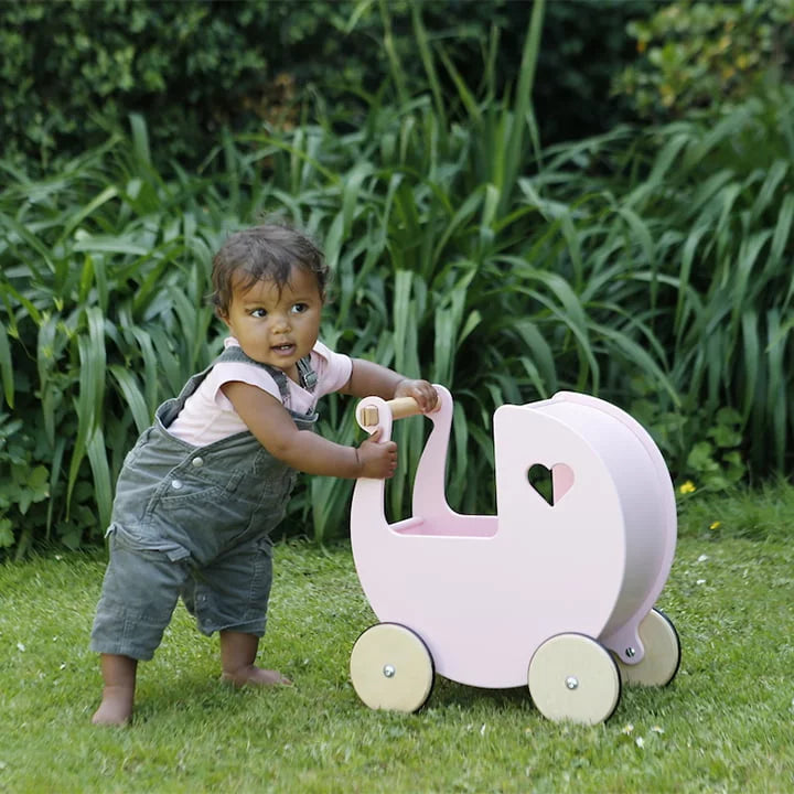 Child playing with a pink toy pram in a garden setting