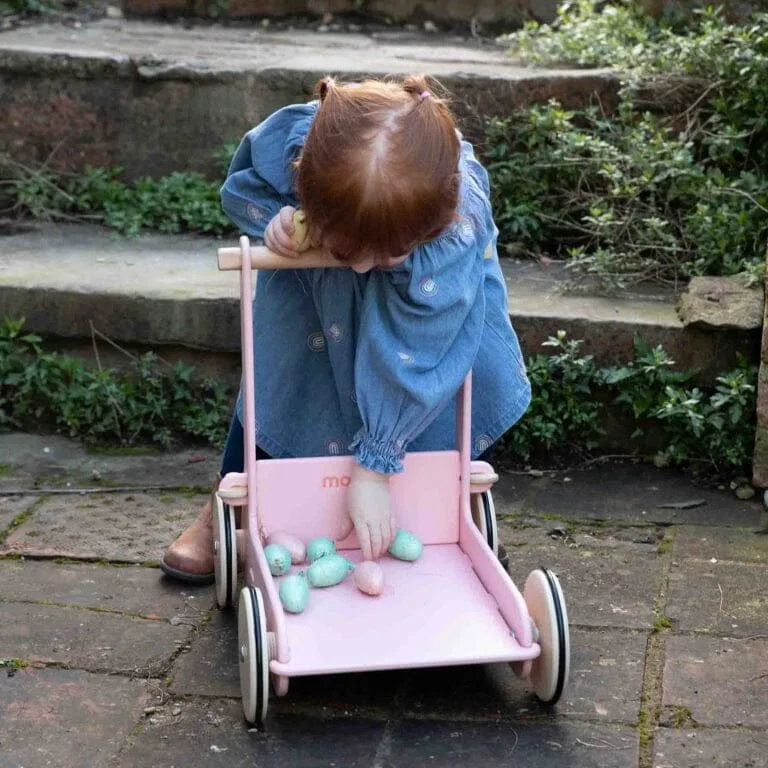 Child playing with a pink doll stroller outdoors