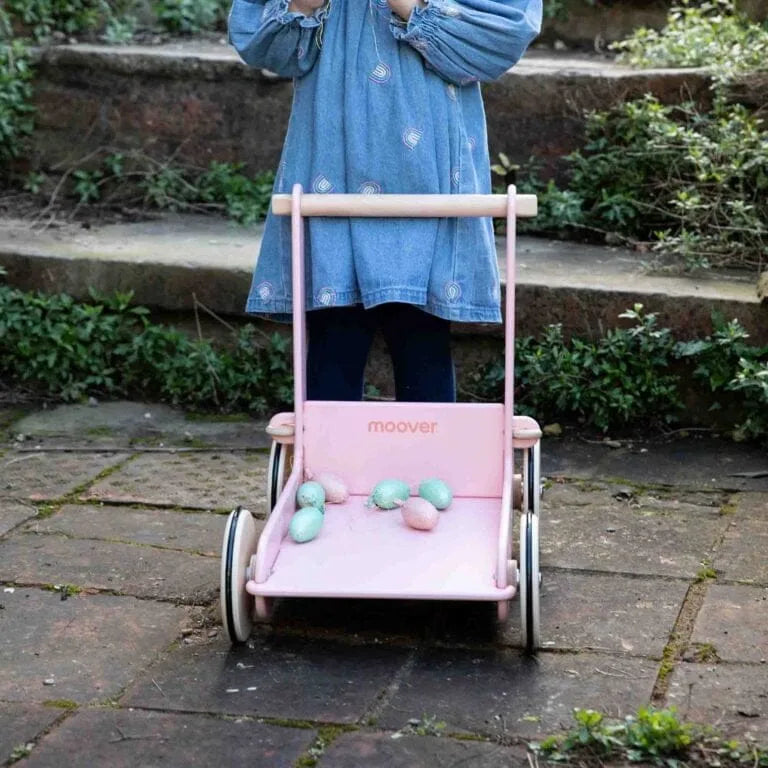 Person pushing a pink toy stroller with 'moover' branding on a stone path.