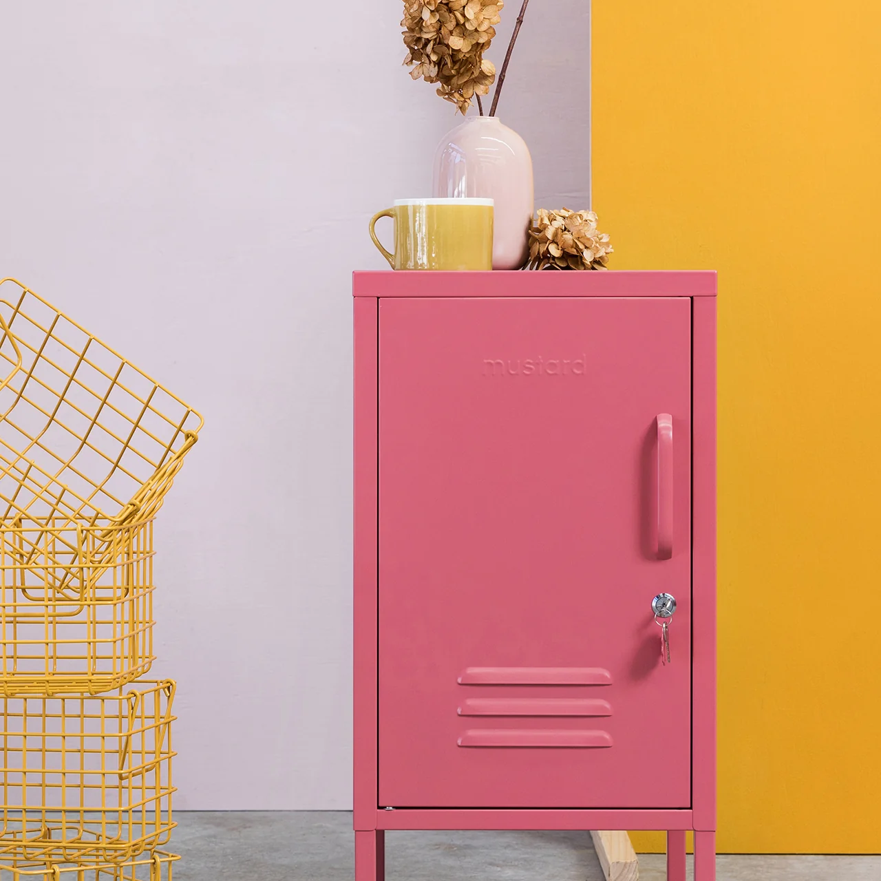 Pink metal cabinet with yellow wire basket against a colorful wall.