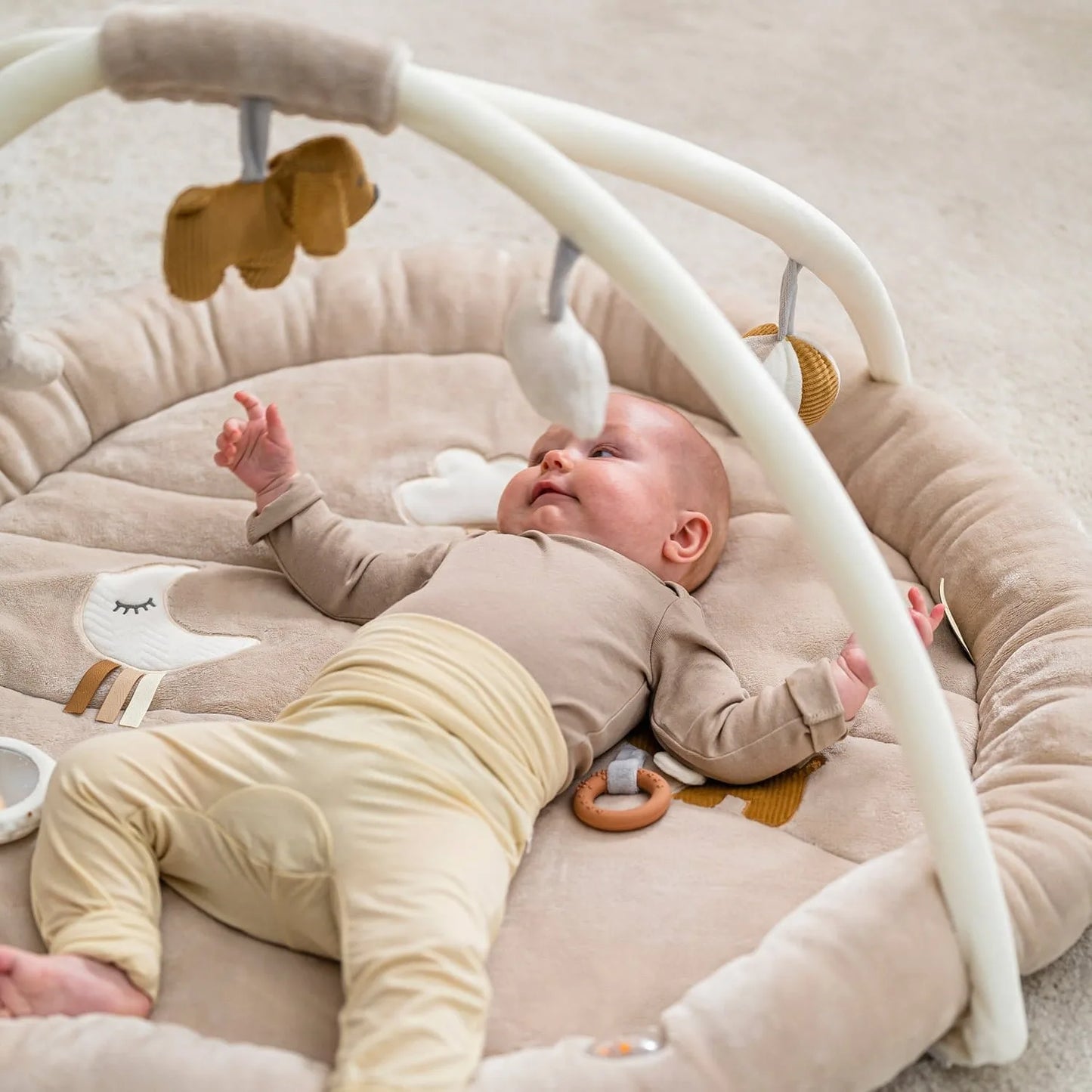 Baby lying on a soft surface with a baby bouncer and toys