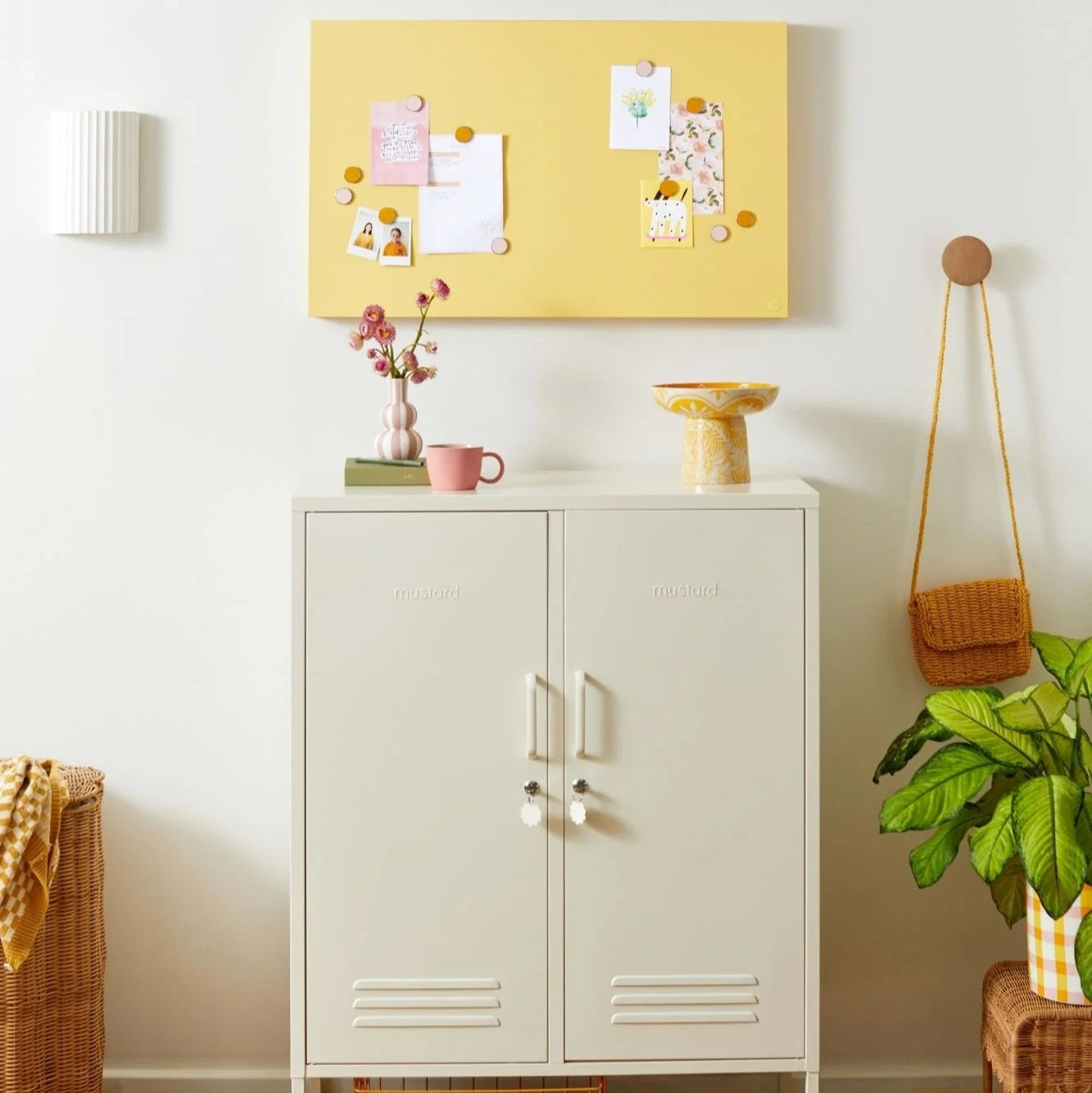 White cabinet with a yellow bulletin board above it in a room with a plant and basket.