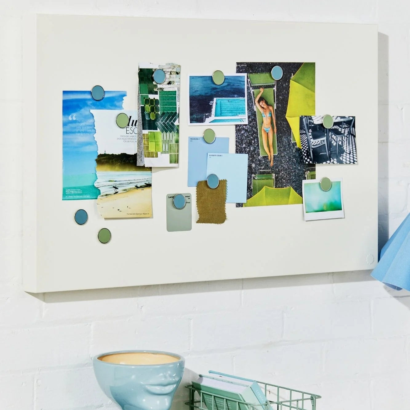 Collage of photos on a white wall above a desk with books and a basket.