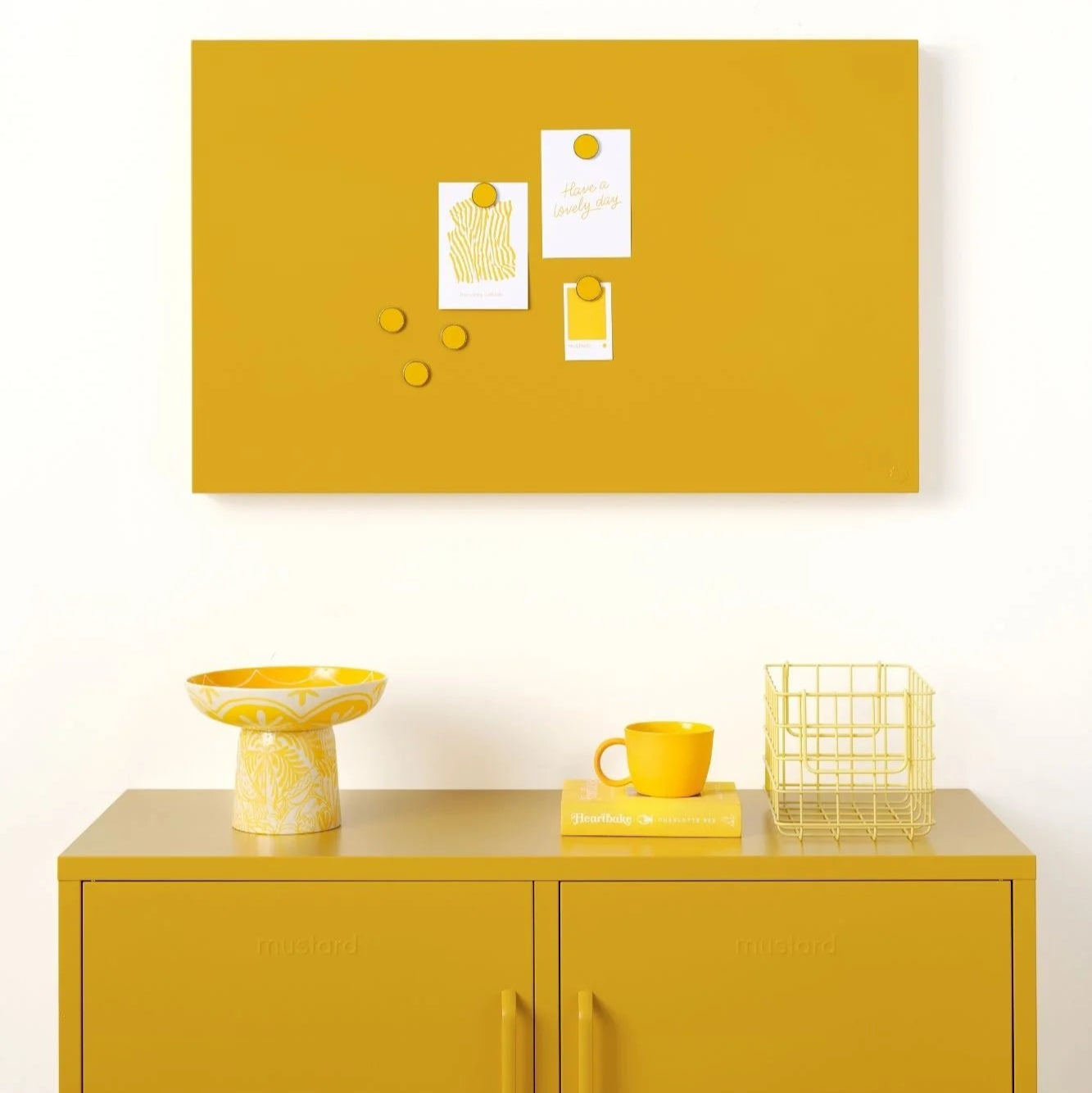 Yellow cabinet with a matching yellow bulletin board above it on a white wall.