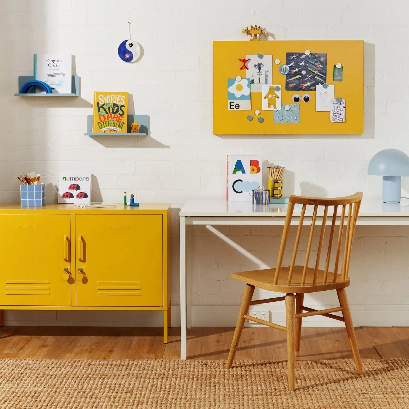 Yellow cabinet, wooden chair, and white desk with colorful decor in a room.