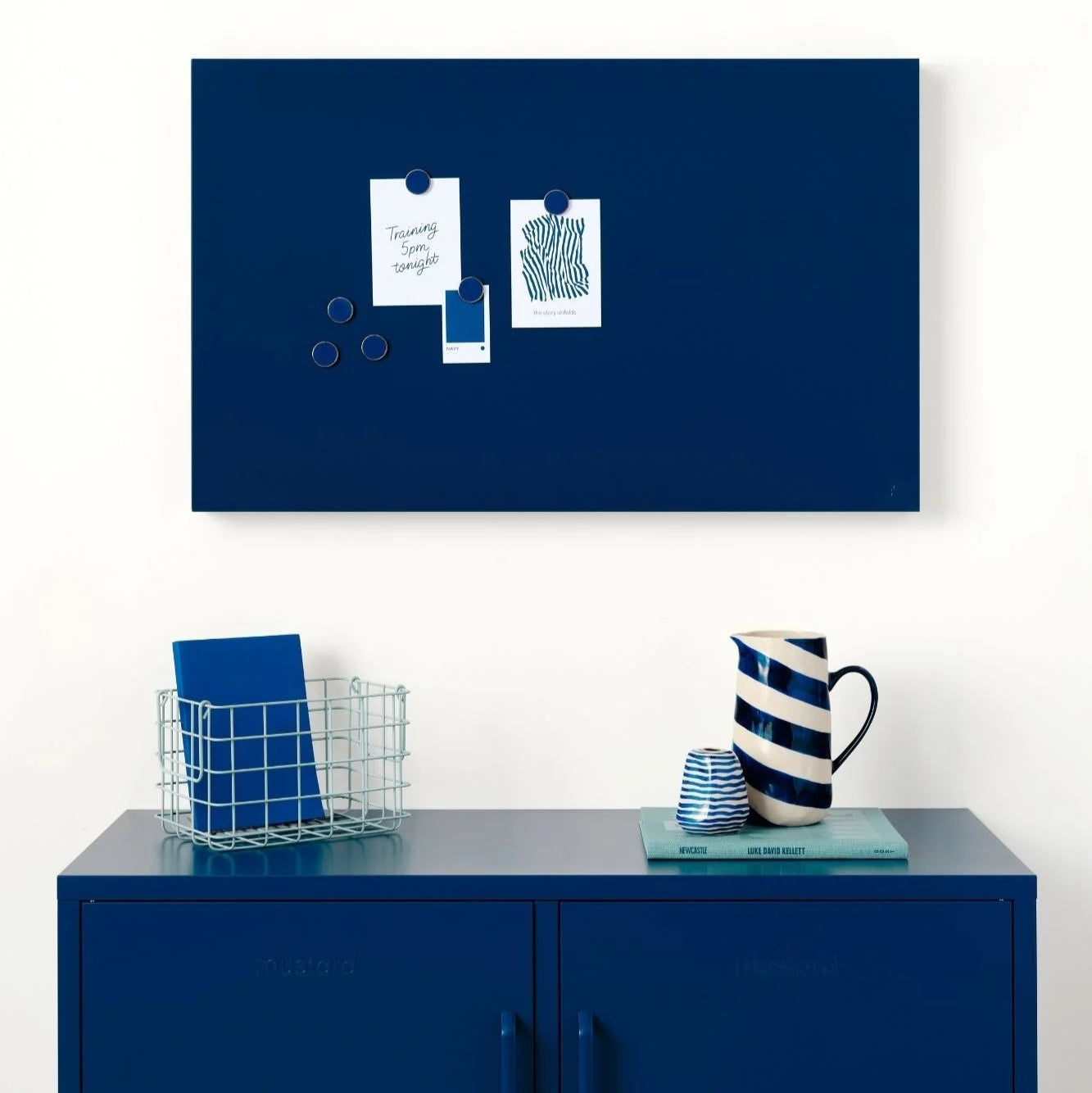 Navy blue magnetic board on a white wall above a blue cabinet with decorative items.