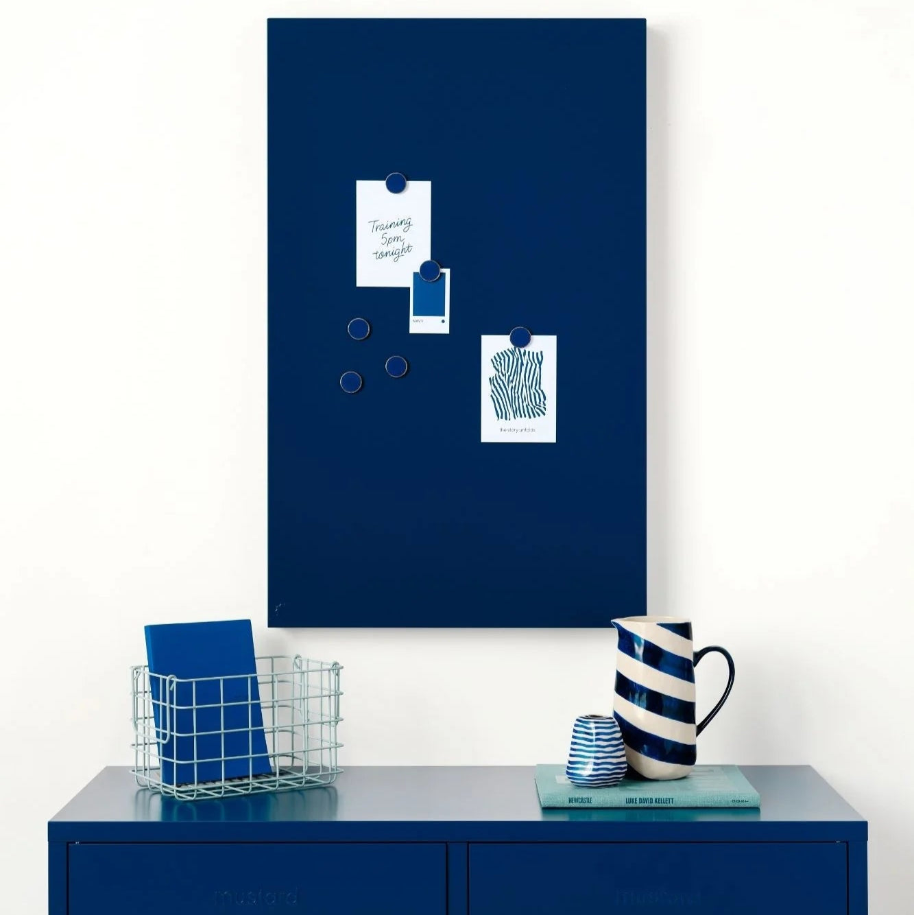 Blue magnetic board on a white wall above a blue cabinet with decorative items.