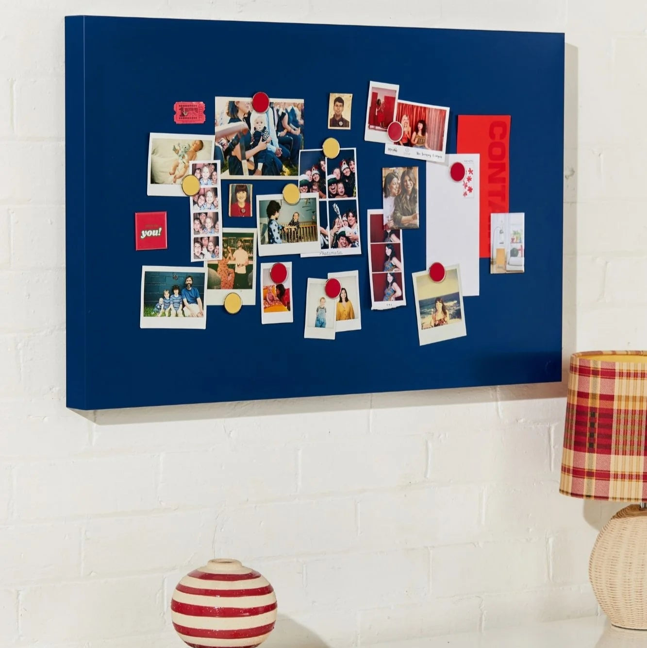 Blue bulletin board with photos and notes on a white wall above a desk.