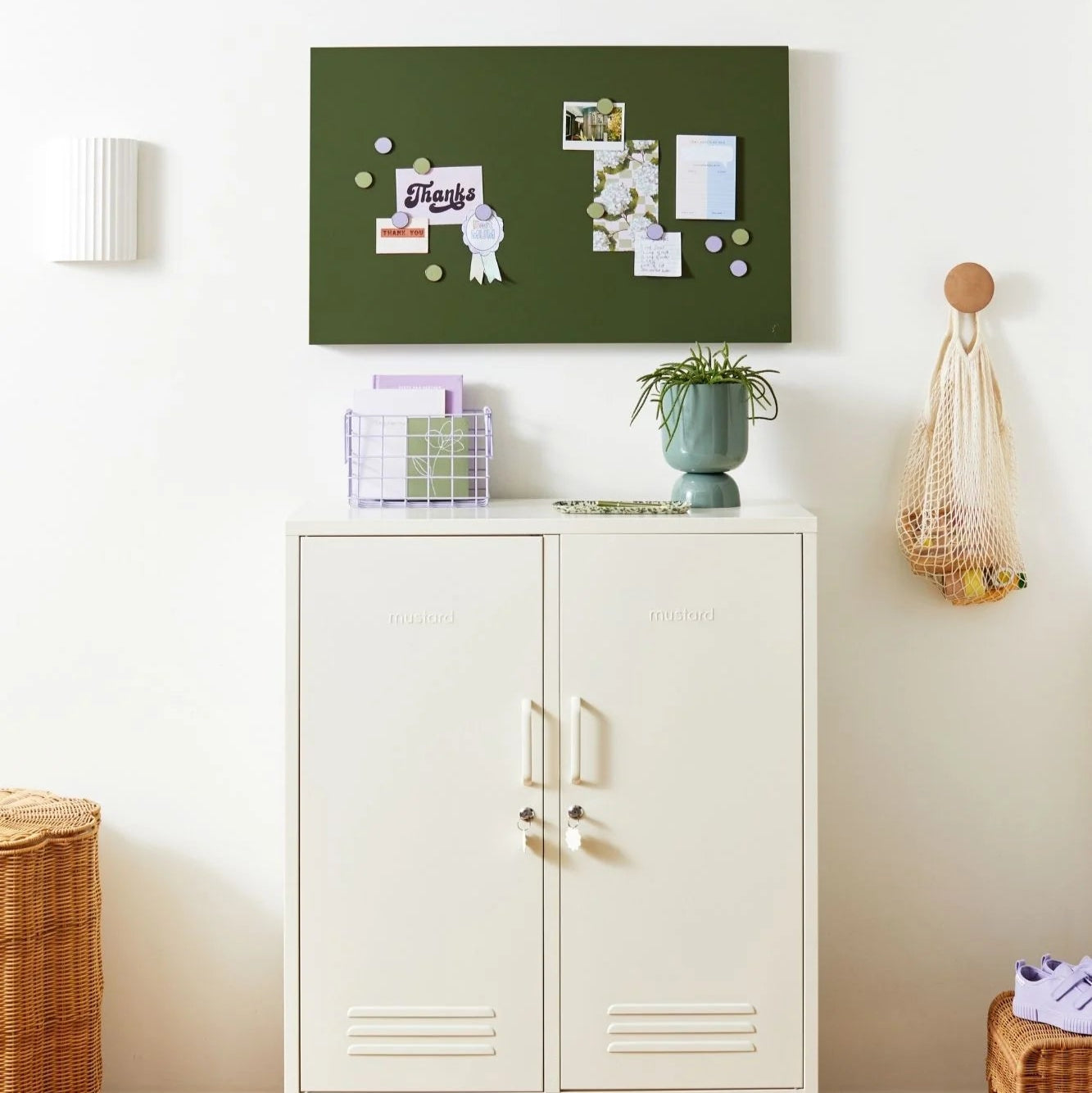 White cabinet with a green bulletin board above it in a room with wooden flooring.