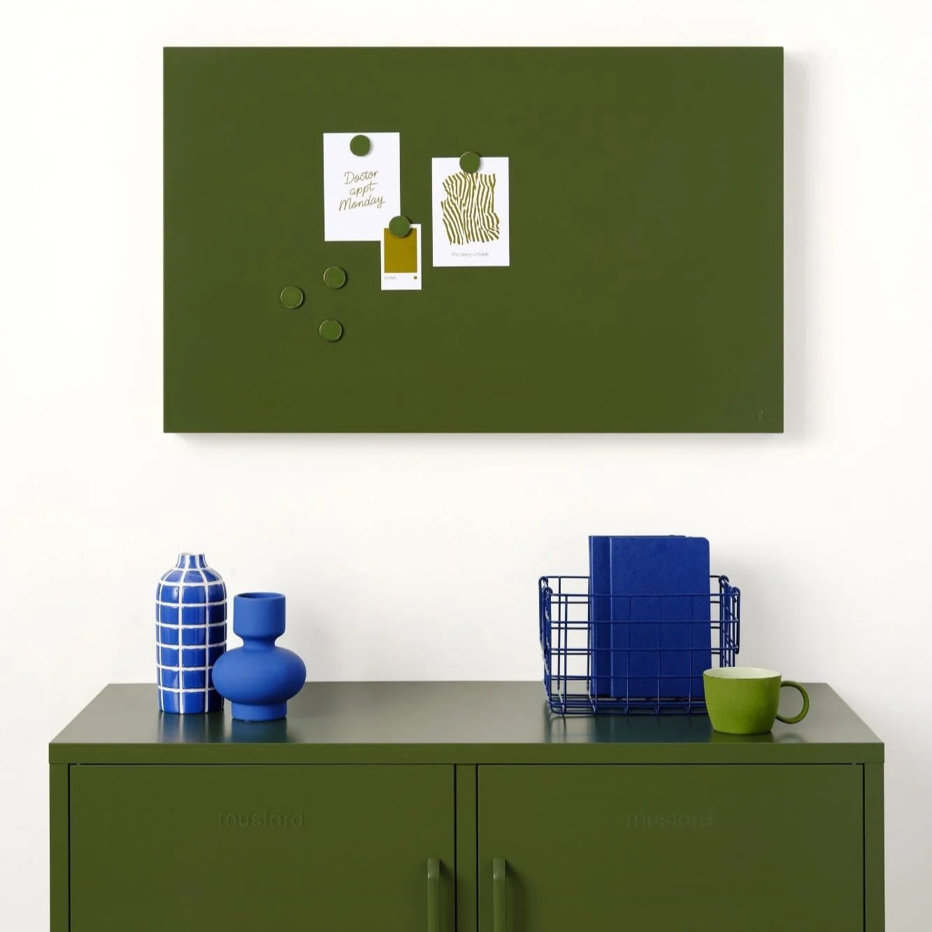 Green magnetic notice board above a green cabinet with decorative items.