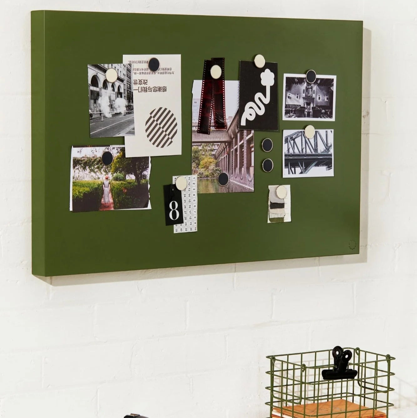 Green magnetic board with photos and notes on a white surface with a camera and laptop.