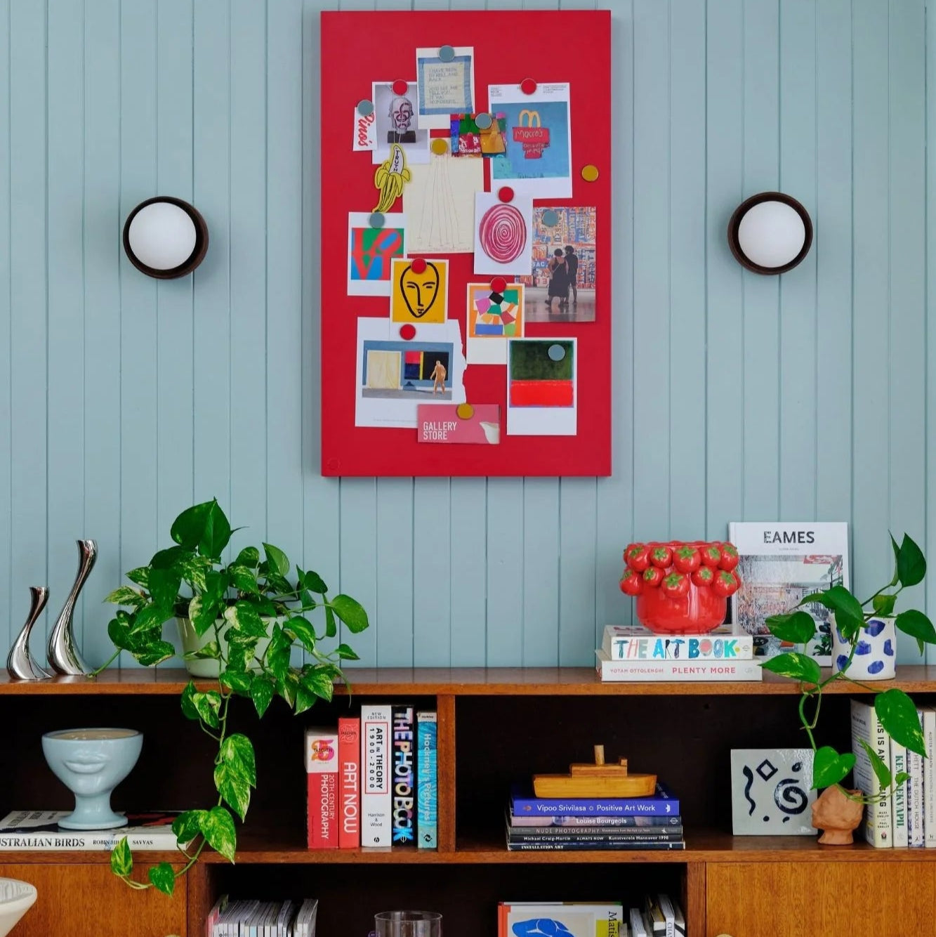 Wooden bookshelf with books and decorative items against a light blue wall with a red collage.
