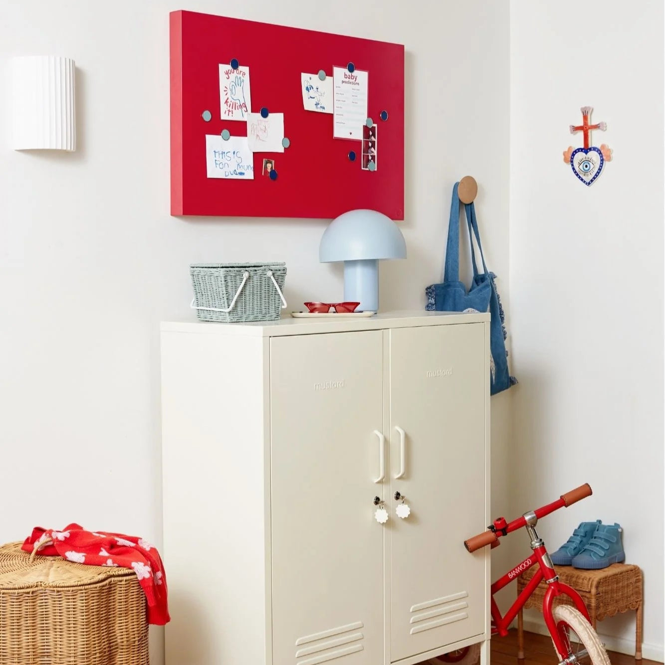Children's room with a white cabinet, red bicycle, and red bulletin board on a white wall.
