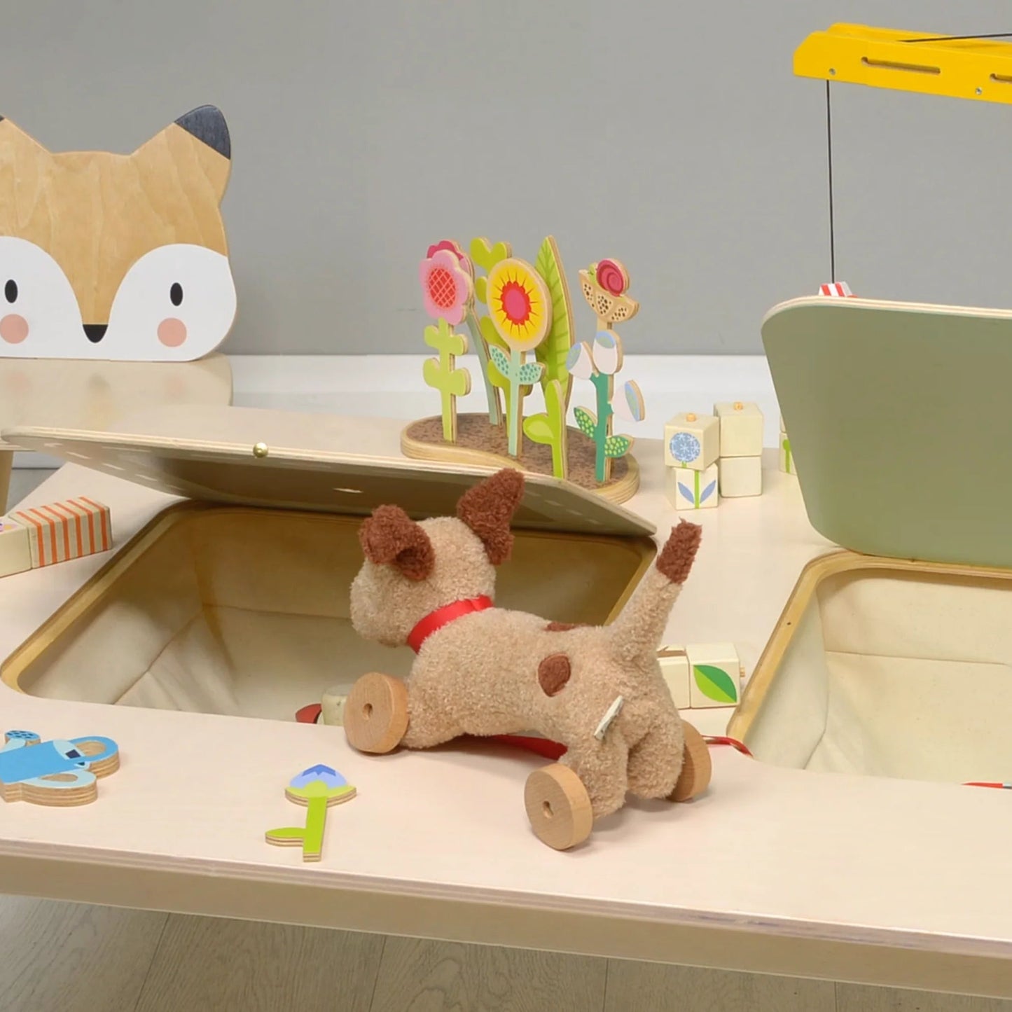 Children's play area with a toy cat, flowers, and a wooden toy car on a light surface.