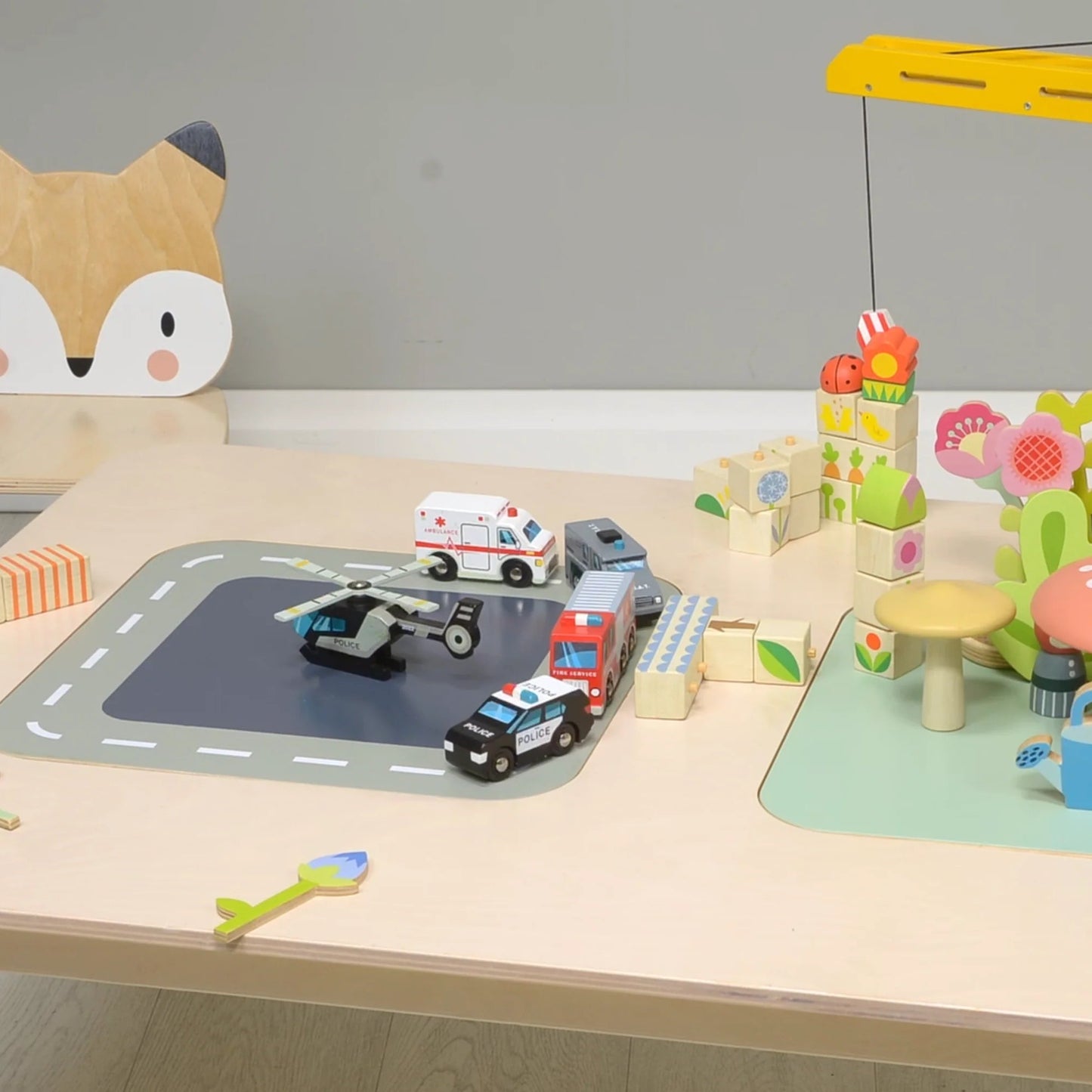 Children's play area with toy cars, blocks, and a fox-shaped cushion on a wooden table.