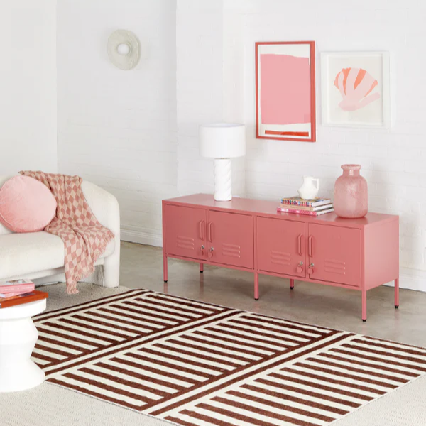 Modern living room with a pink sideboard, striped rug, and abstract art on white walls.