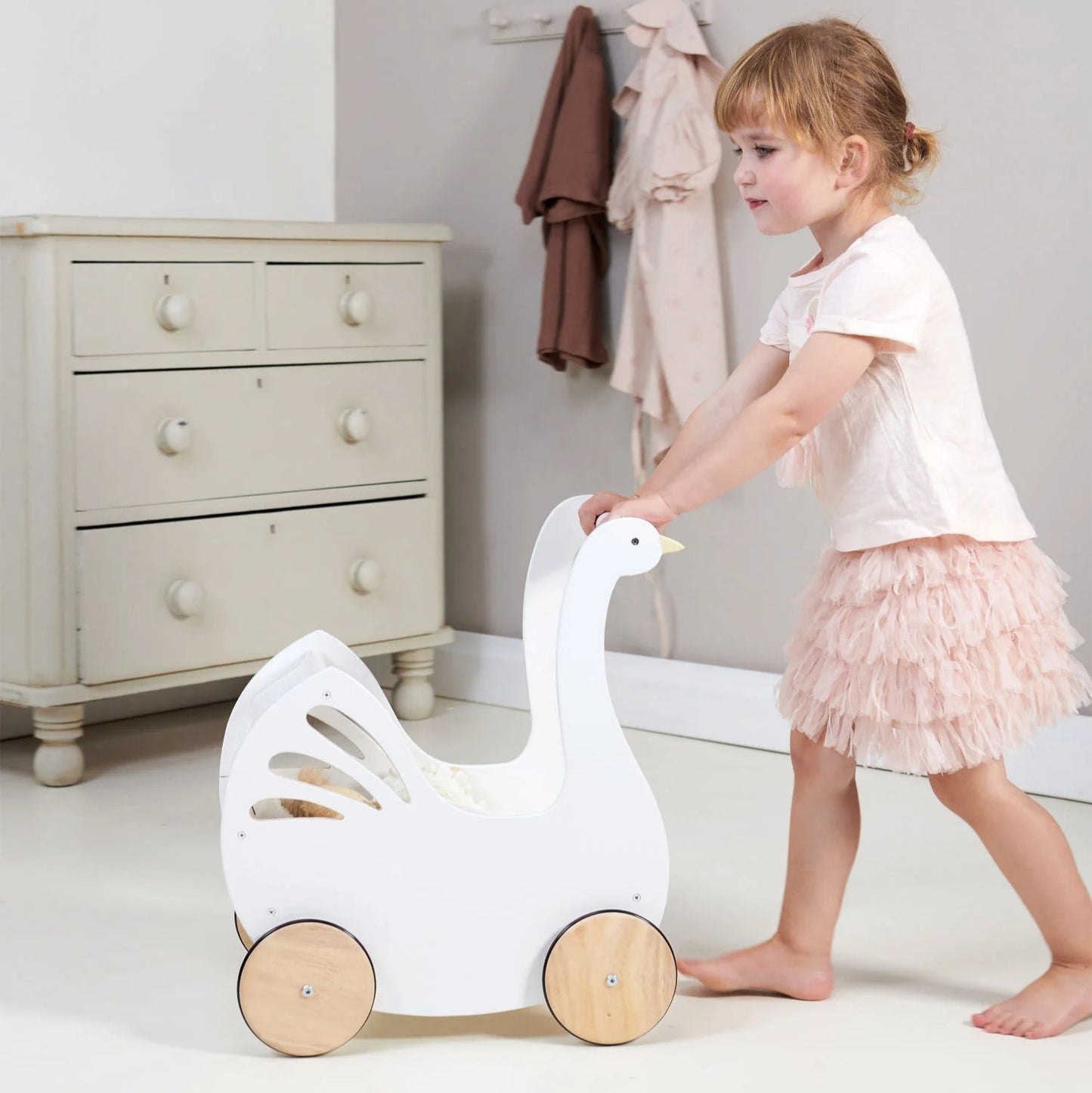 Child playing with a white goose-shaped toy in a room with a dresser and clothes in the background.
