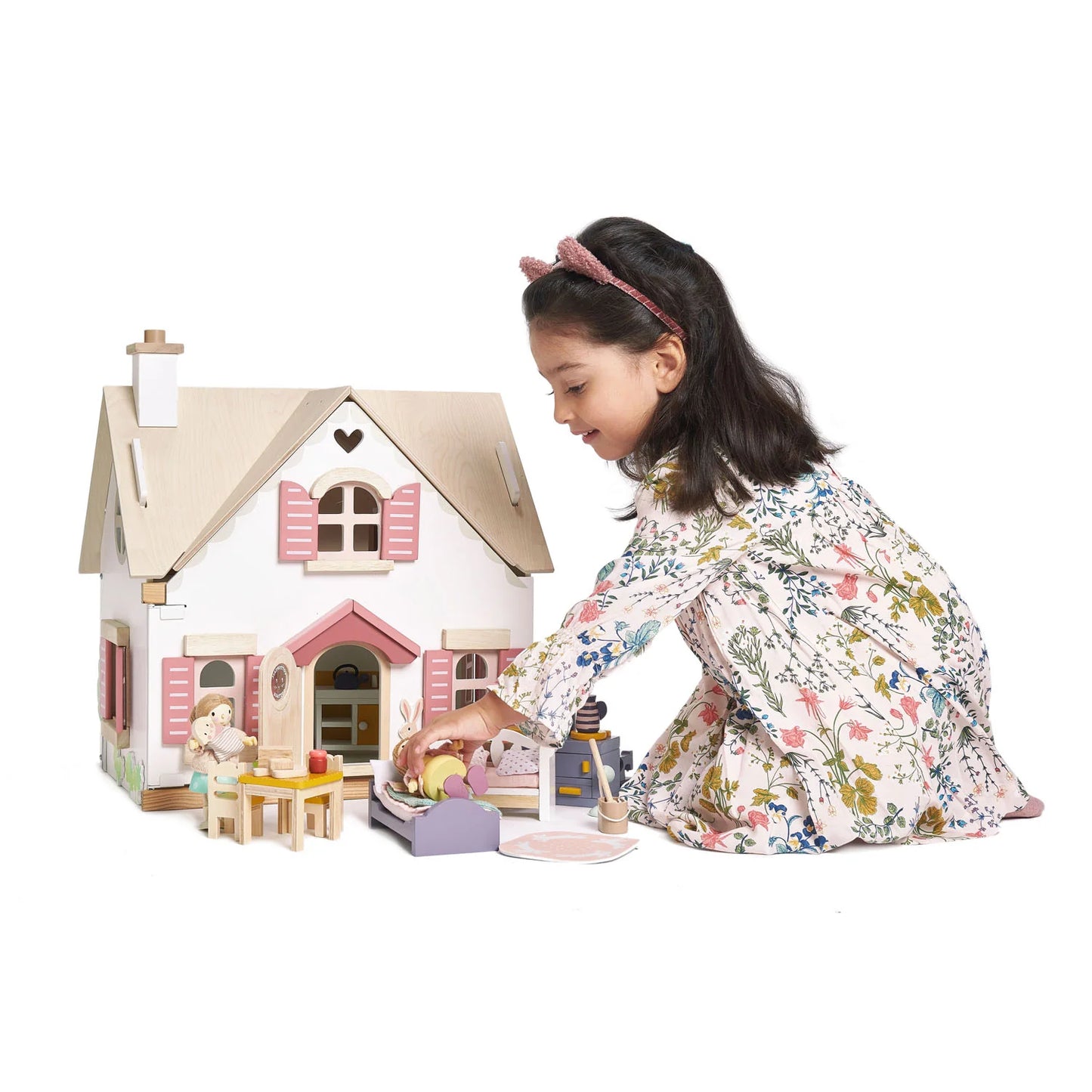 Young girl playing with a dollhouse and accessories on a white background