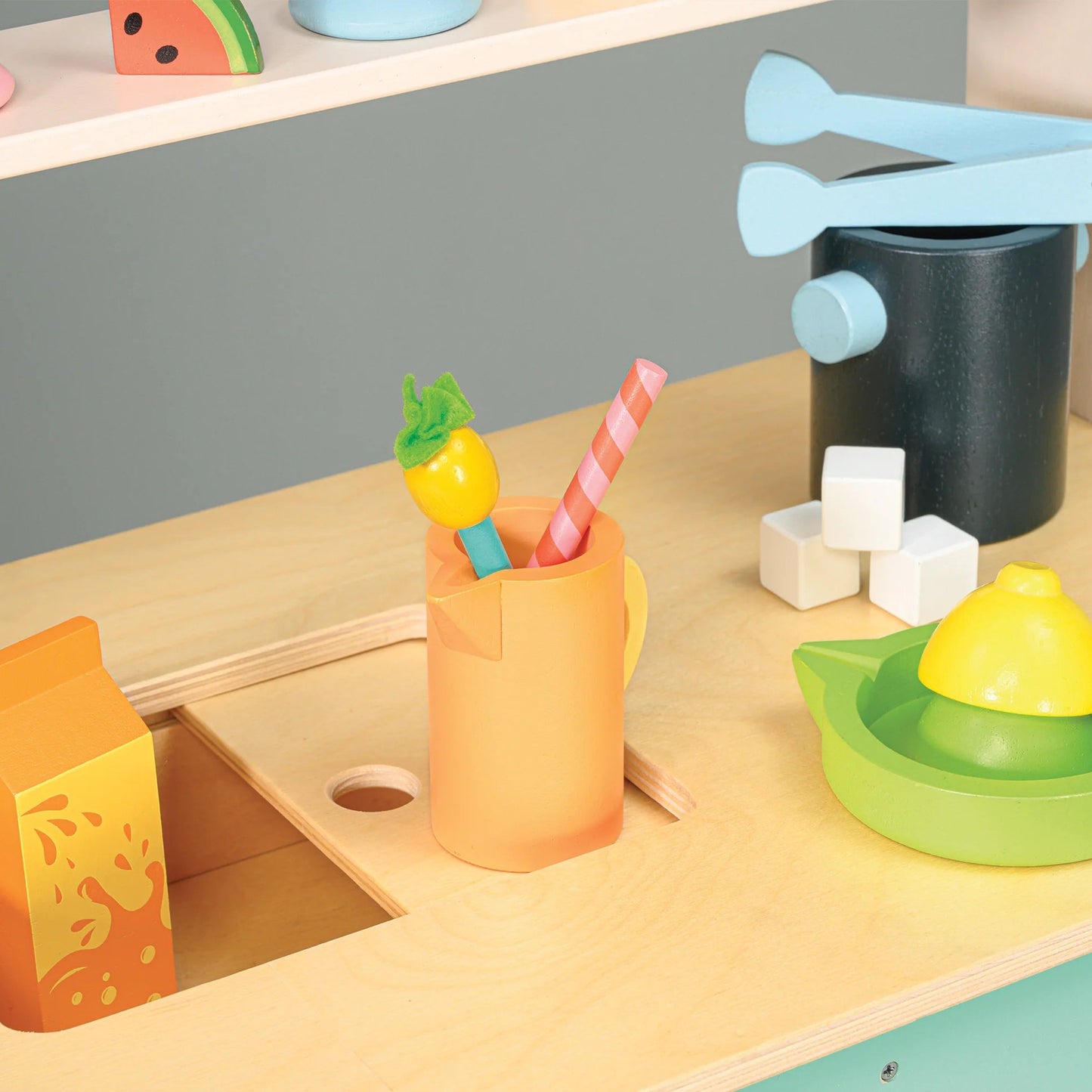 Colorful toy kitchen set with sink, cups, and utensils on a wooden surface.