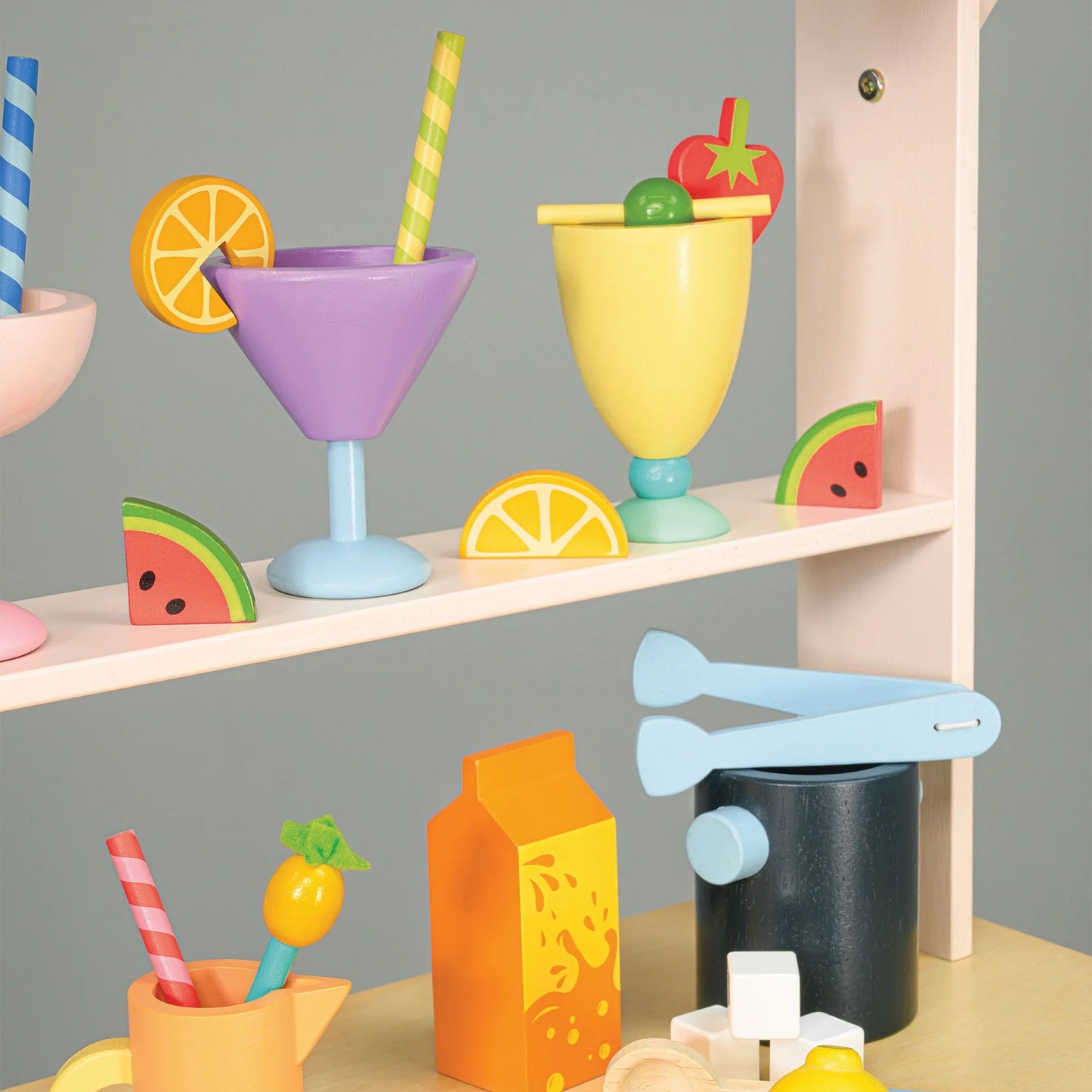 Children's play kitchen set with colorful cups, bottles, and utensils on a wooden surface.